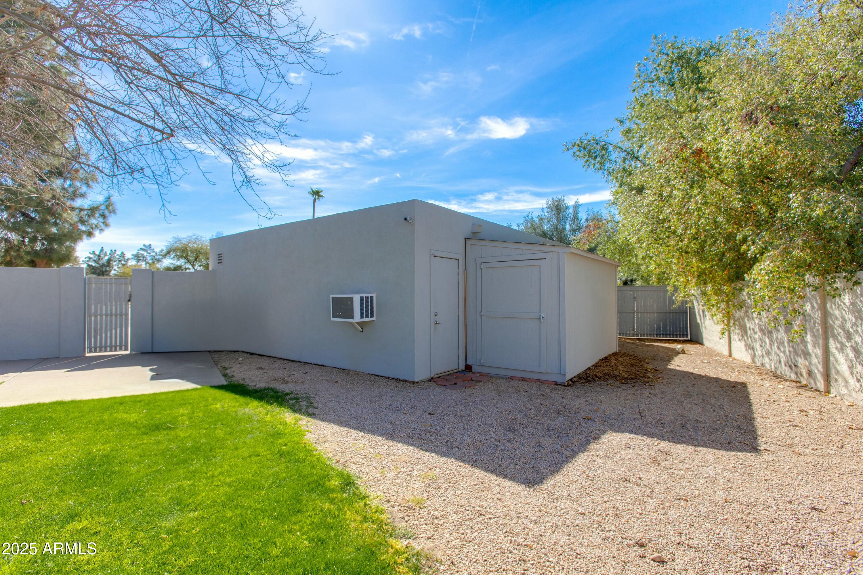 Backyard with a gray outbuilding, gravel landscaping, green lawn, and perimeter walls.
