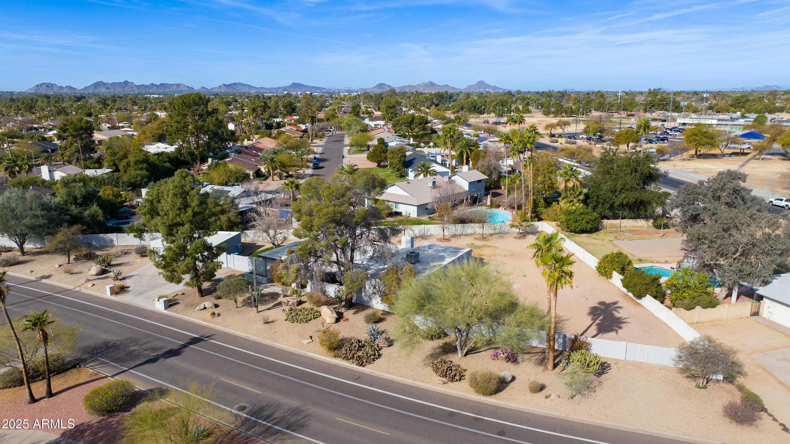 Aerial view of a Scottsdale home with desert landscaping, neighboring pools, and mountains on the horizon.