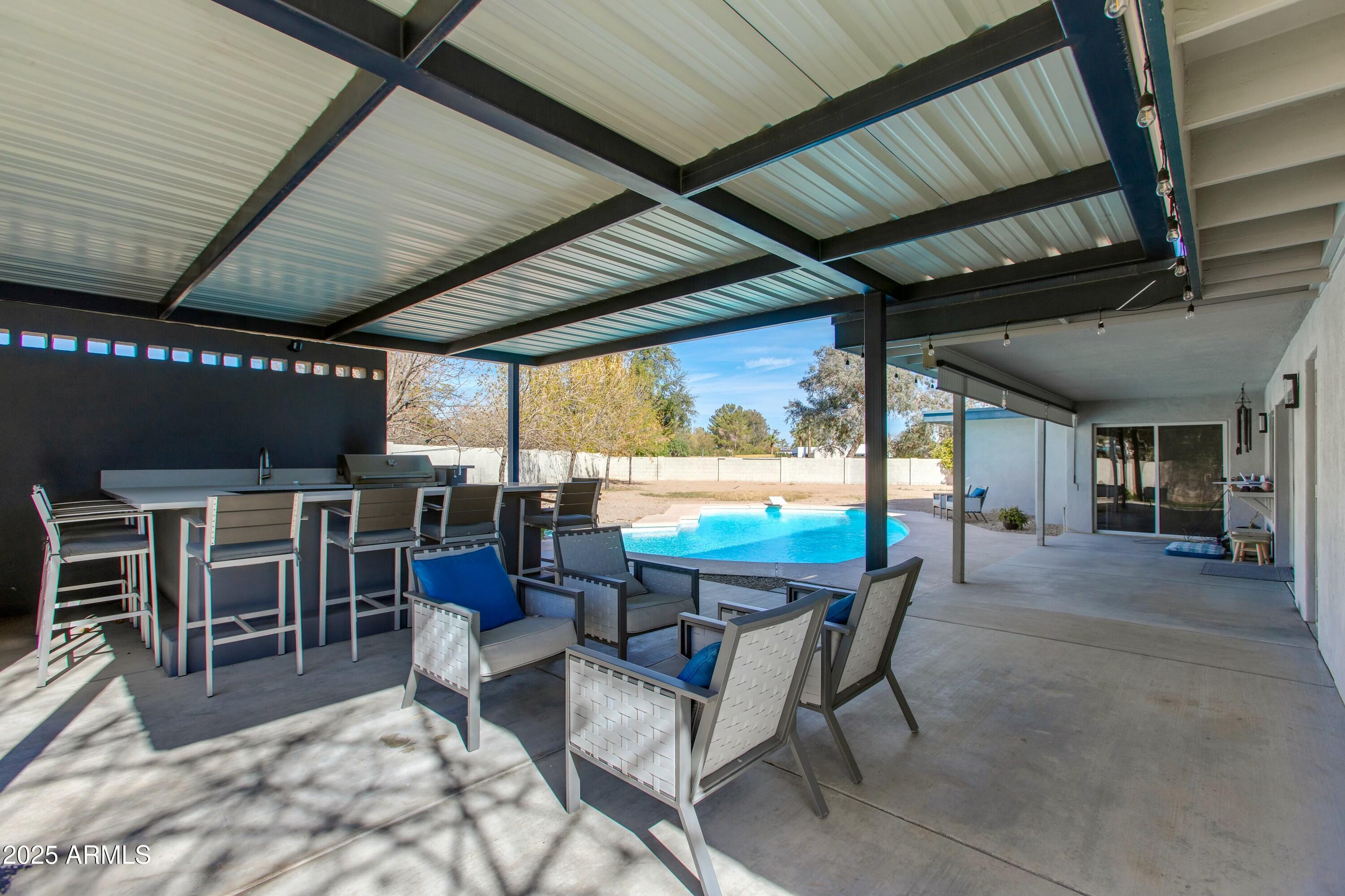 Covered patio with lounge seating and an outdoor bar overlooking a swimming pool.
