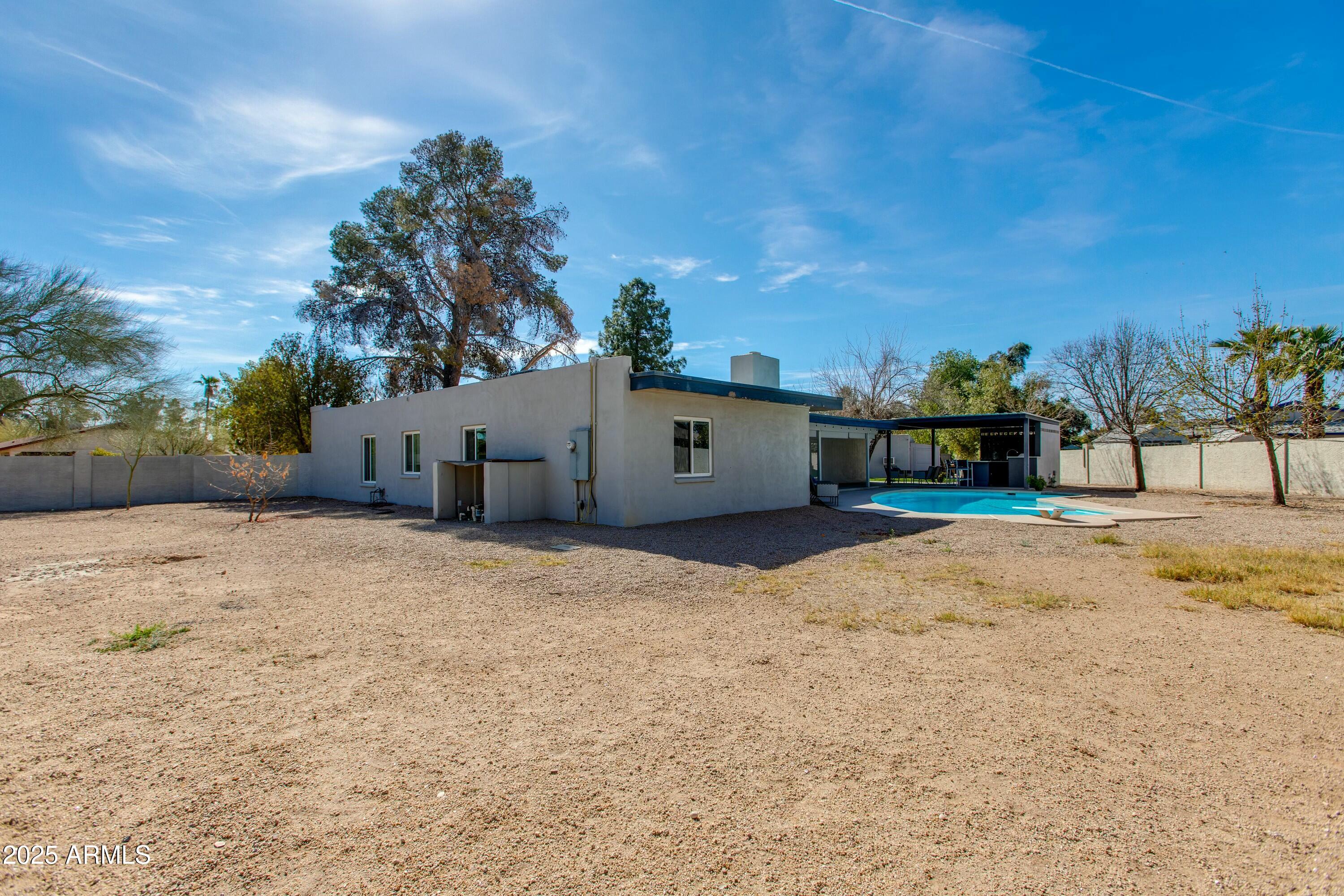 Home’s rear exterior with a covered patio, swimming pool, and spacious gravel yard.