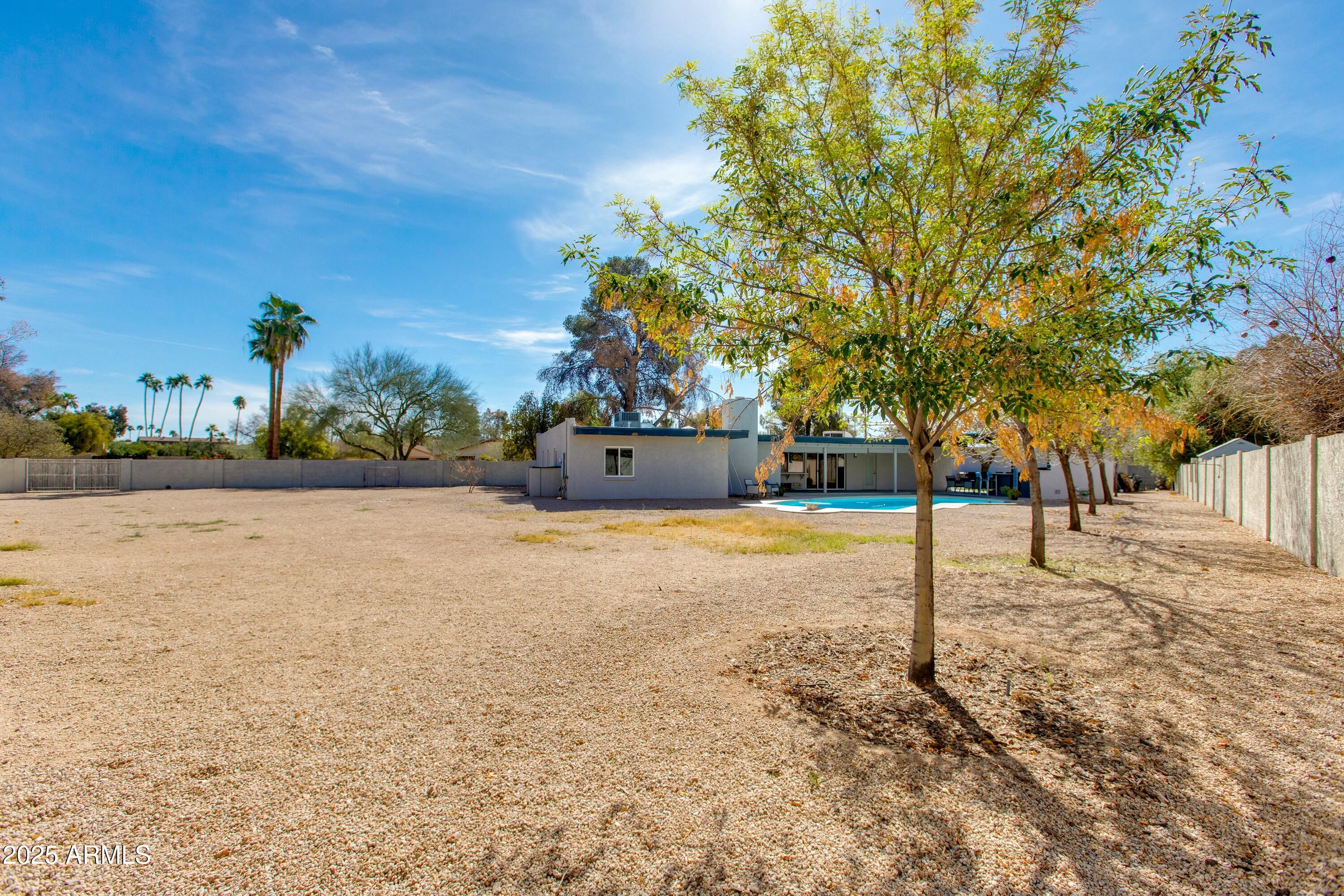 Spacious gravel backyard with a swimming pool, mature trees, and a single-story home.