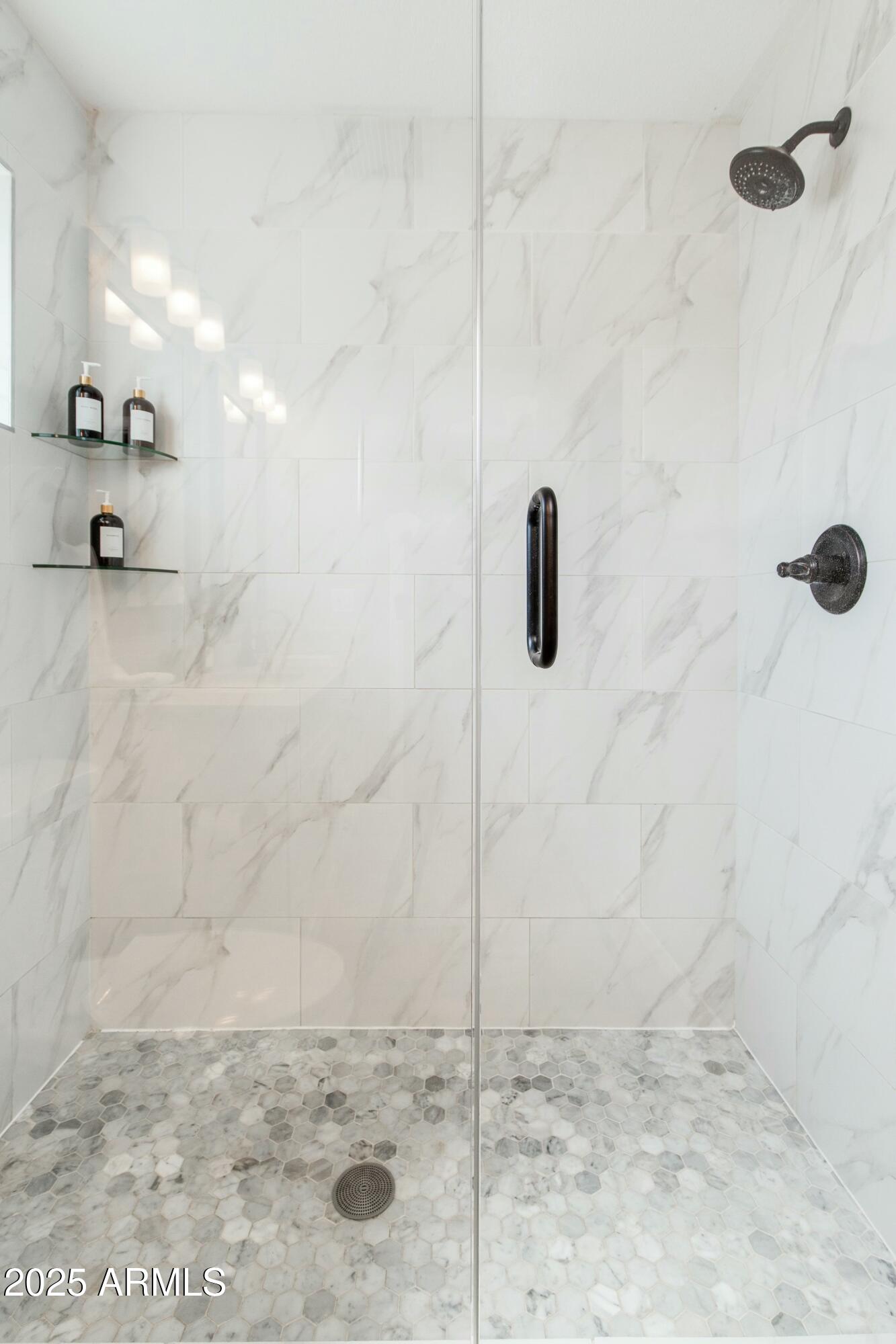 Walk-in shower with marble-look tile, a hexagonal mosaic floor, glass enclosure, and black fixtures.