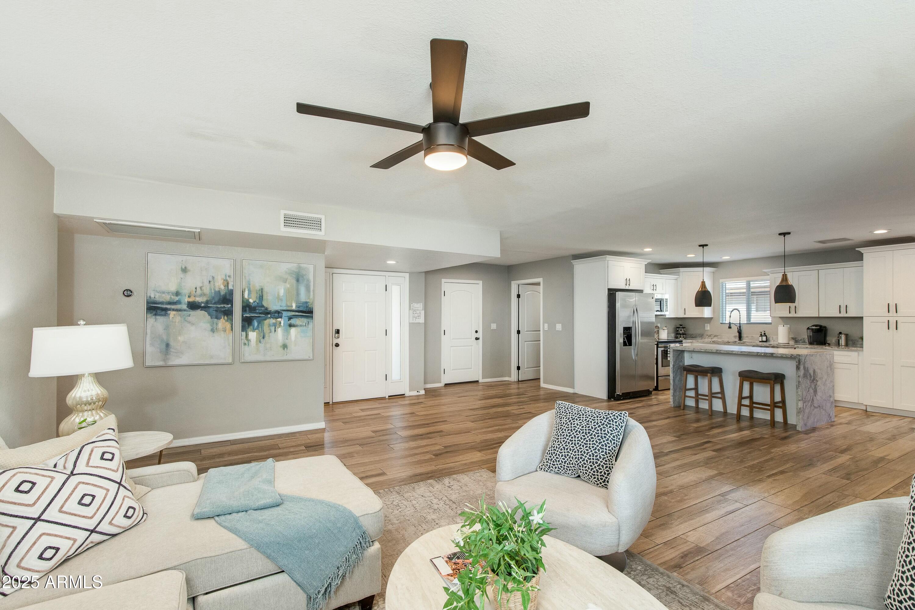 Open-plan living room and kitchen with a stone island, white cabinets, and wood-look floors.