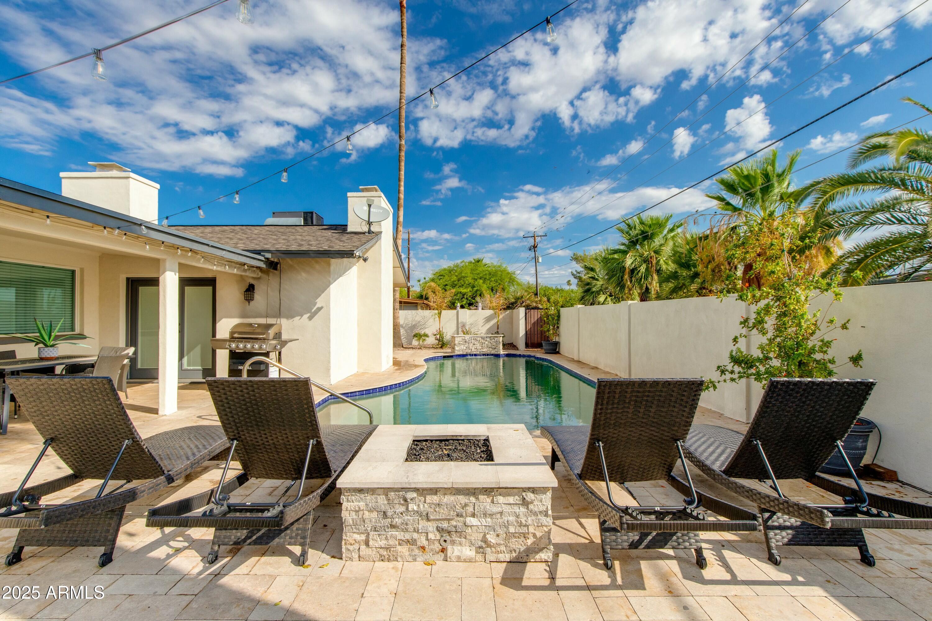 Backyard pool with woven lounge chairs, a stone fire pit, and palm trees.