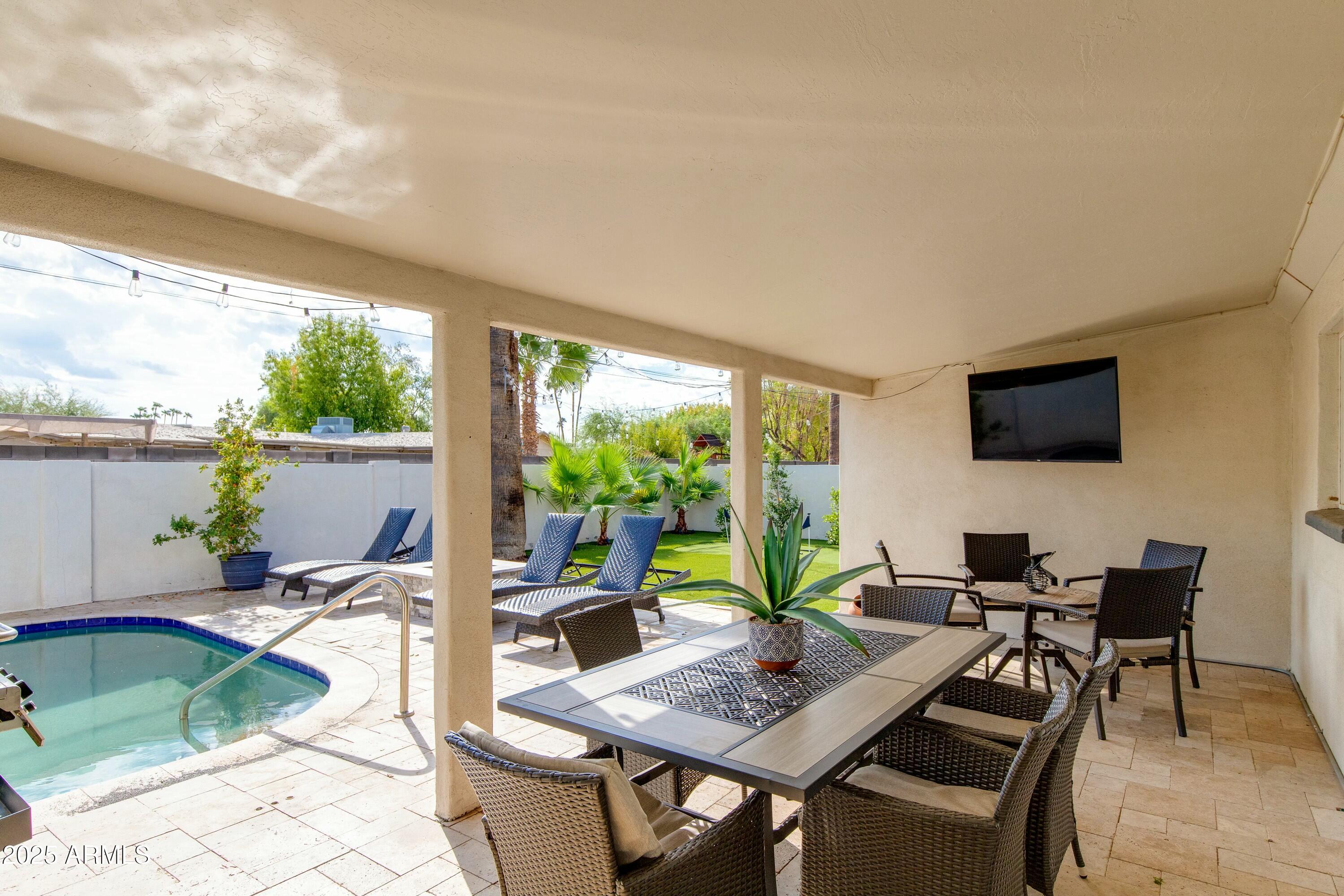 Covered patio with wicker dining set overlooking a swimming pool and landscaped yard.