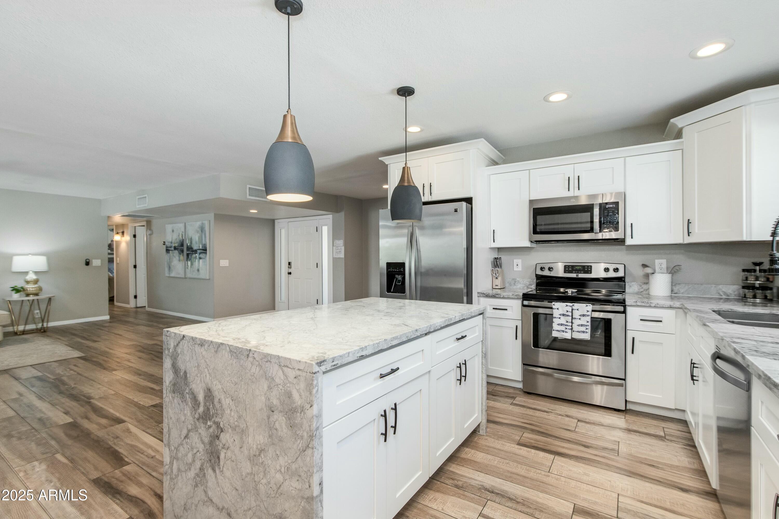 Kitchen with a large marble-patterned island, white cabinets, and stainless steel appliances.