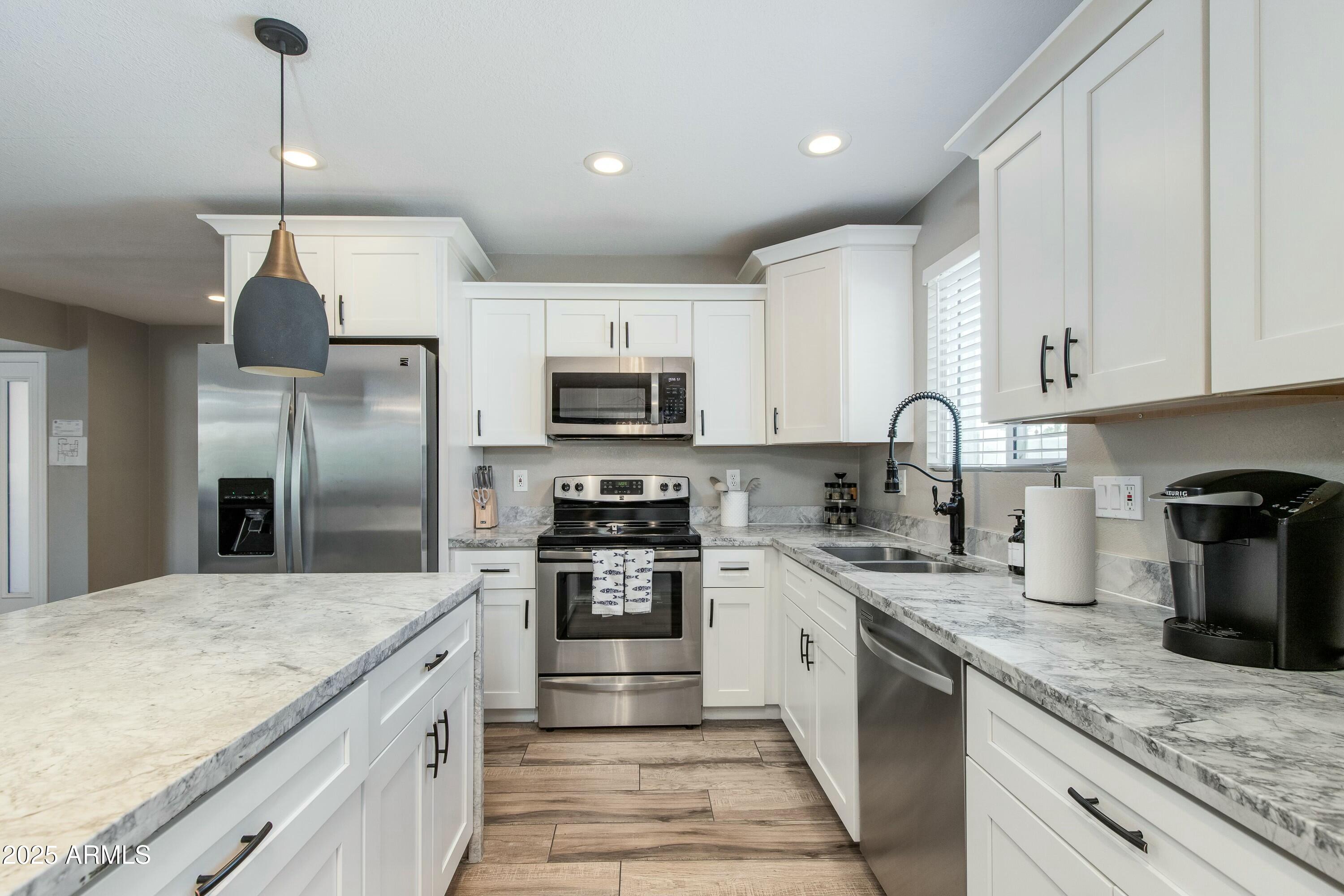 Kitchen with white cabinets, marble-pattern counters, a large island, and stainless steel appliances.