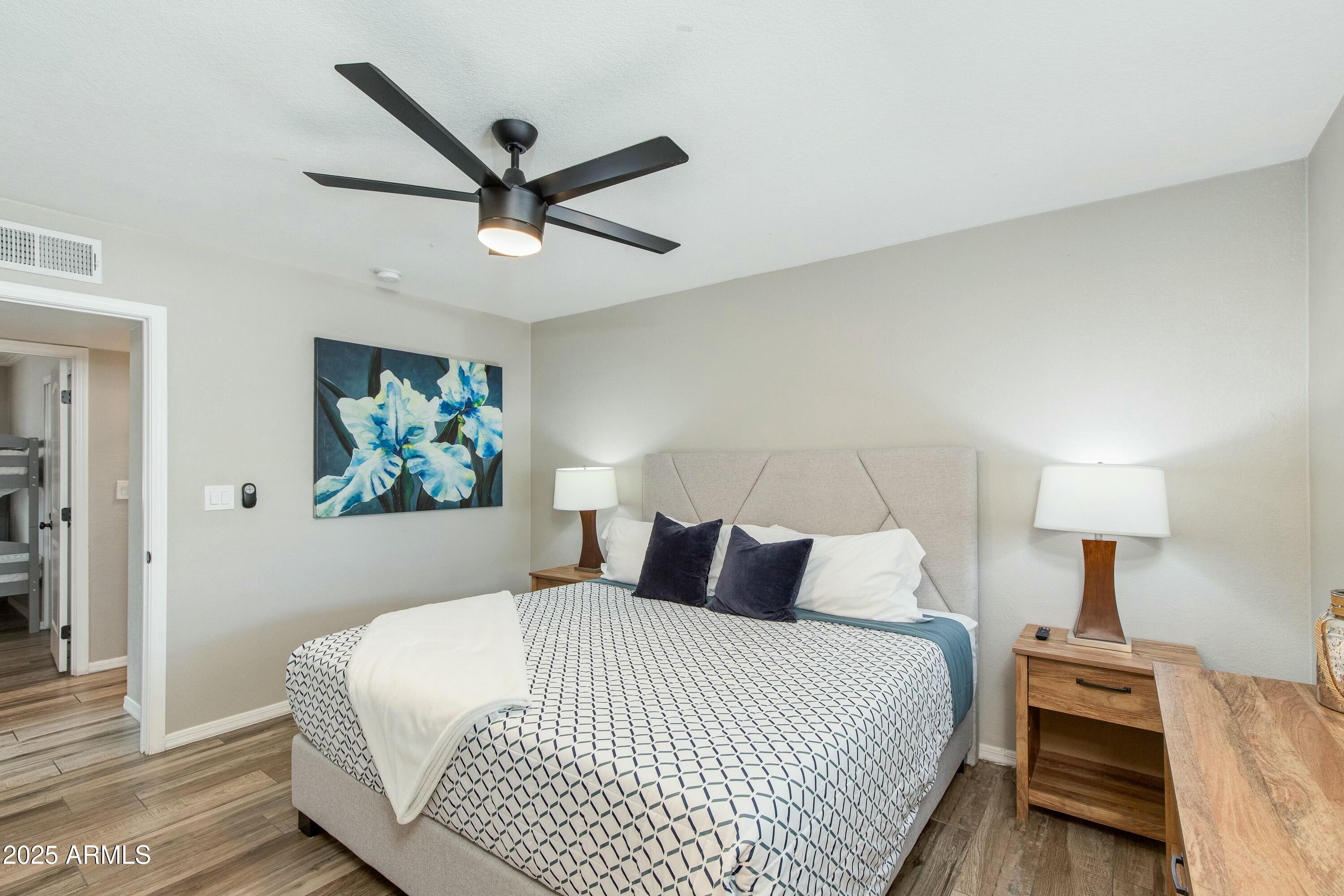 Bedroom with a geometric black-and-white bedspread, blue pillows, and a dark ceiling fan.
