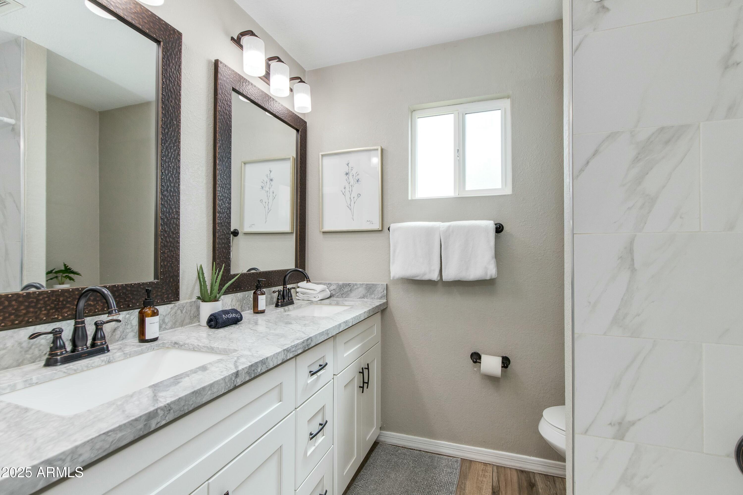Bathroom with a marble double vanity, dark-framed mirrors, black fixtures and a small window.