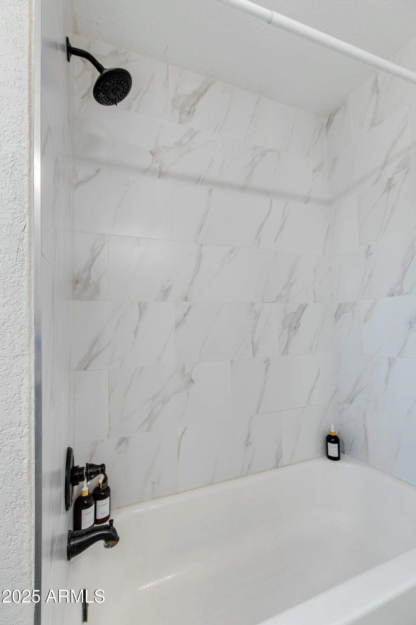 Bathroom tub and shower with marble-look tile and matte black fixtures.