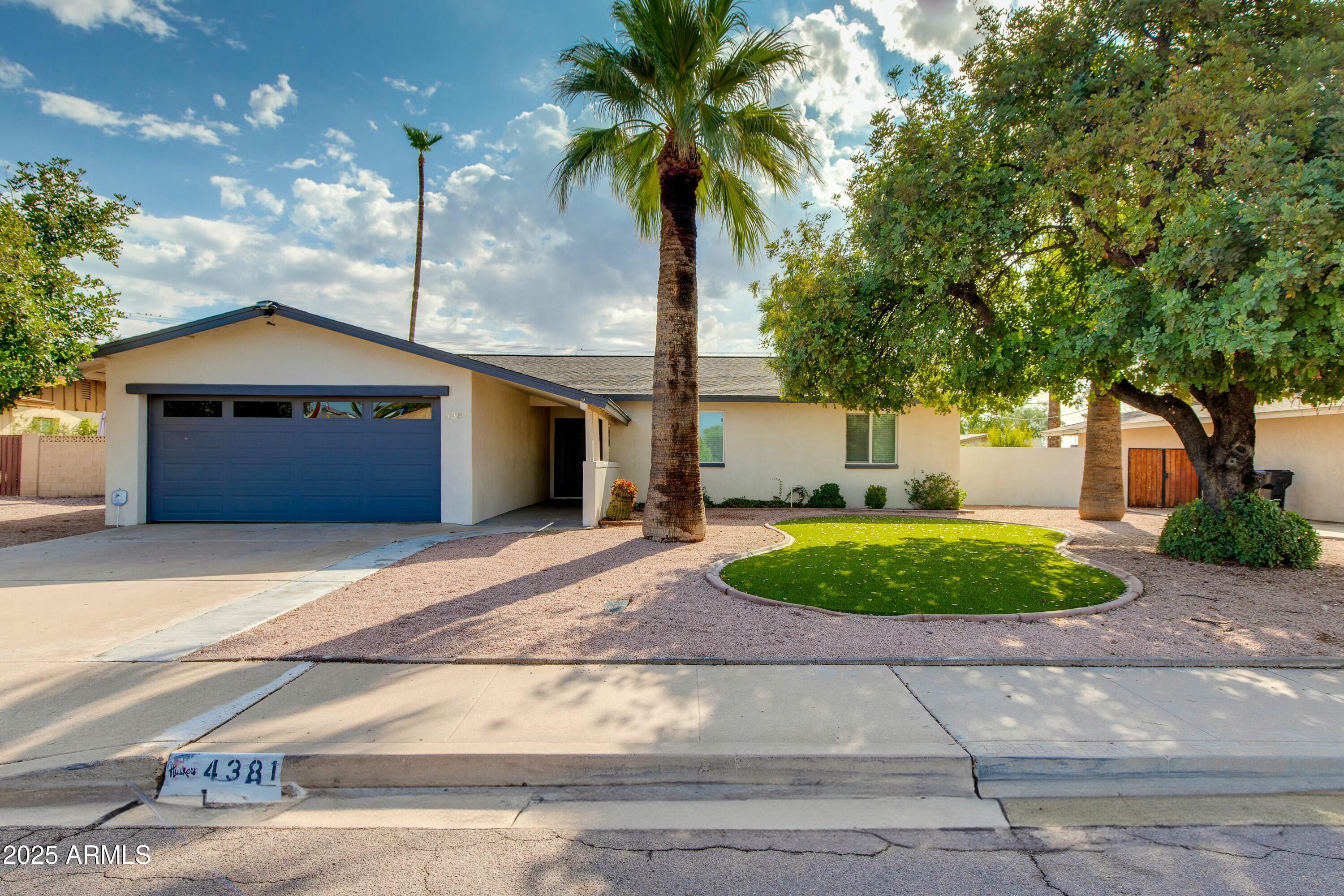 Single-story home with a blue garage door, tall palm trees, and a circular green lawn.