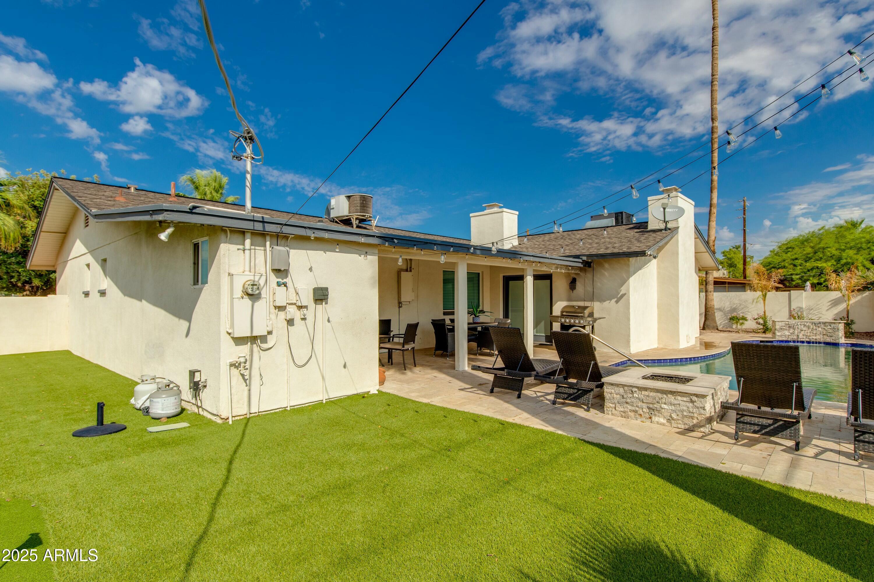 Rear of a single-story home with a covered patio, pool, lounge chairs, and lawn.