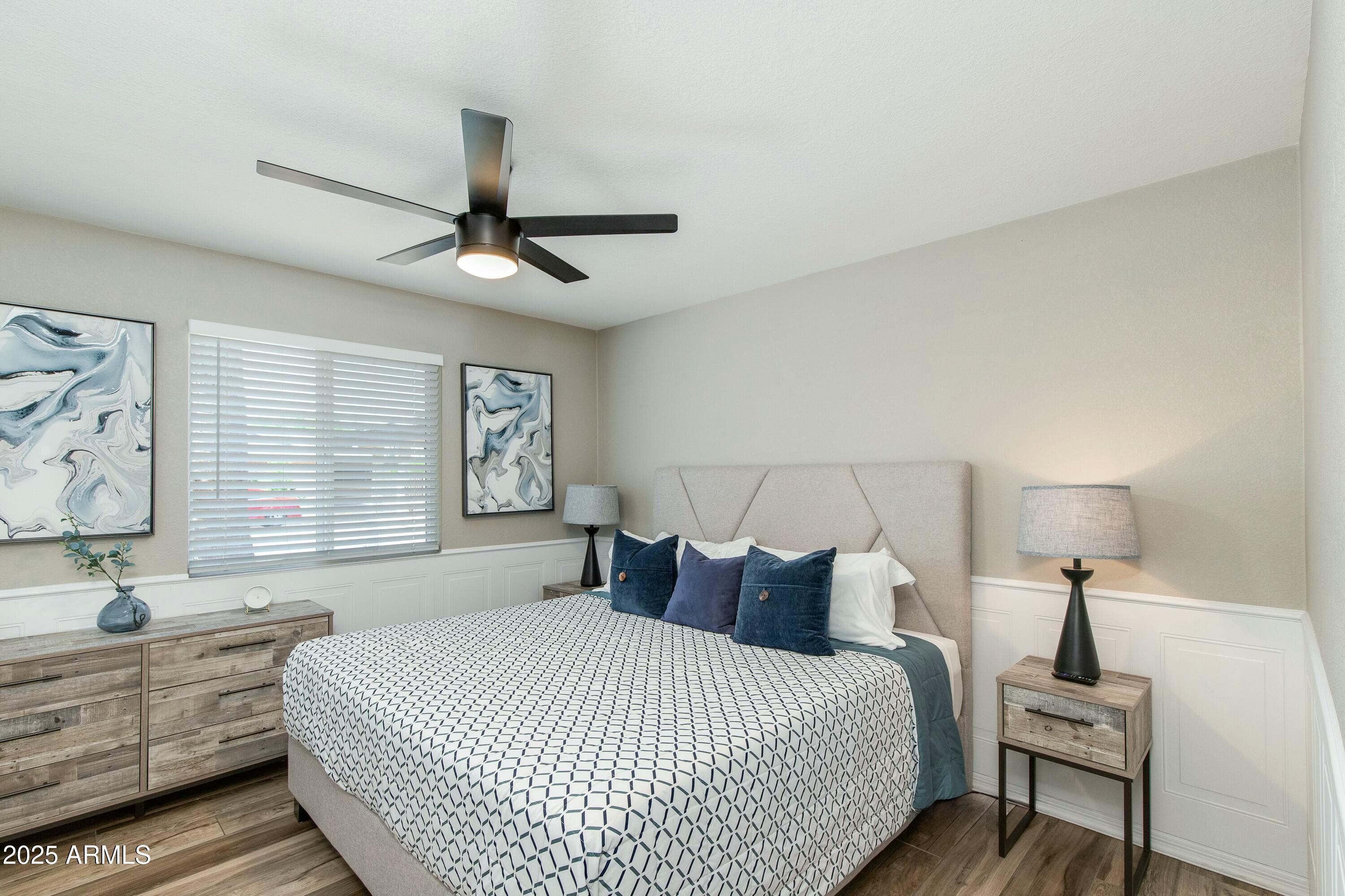 Furnished bedroom with a geometric-patterned bedspread, navy pillows, and a black ceiling fan.