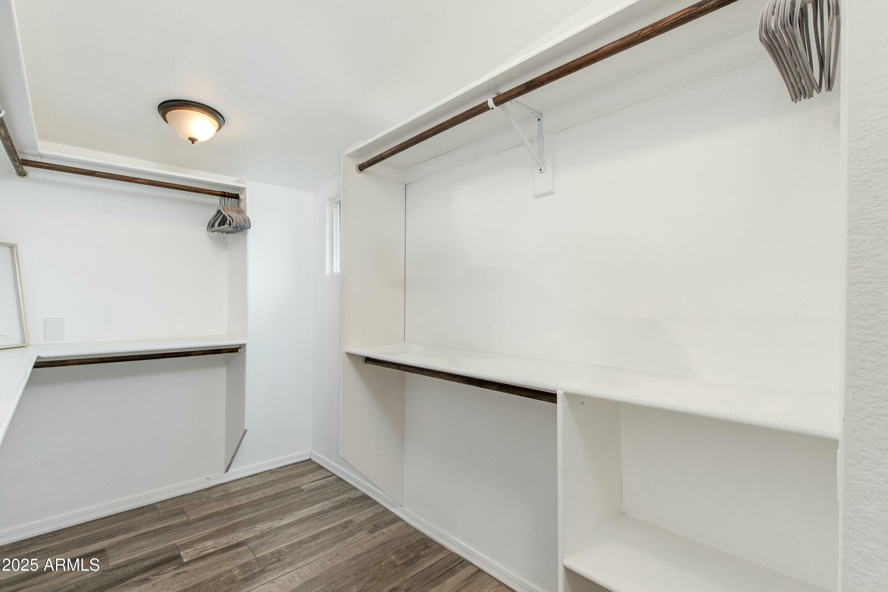 Walk-in closet with white built-in shelving, dark hanging rods, and wood-look flooring.
