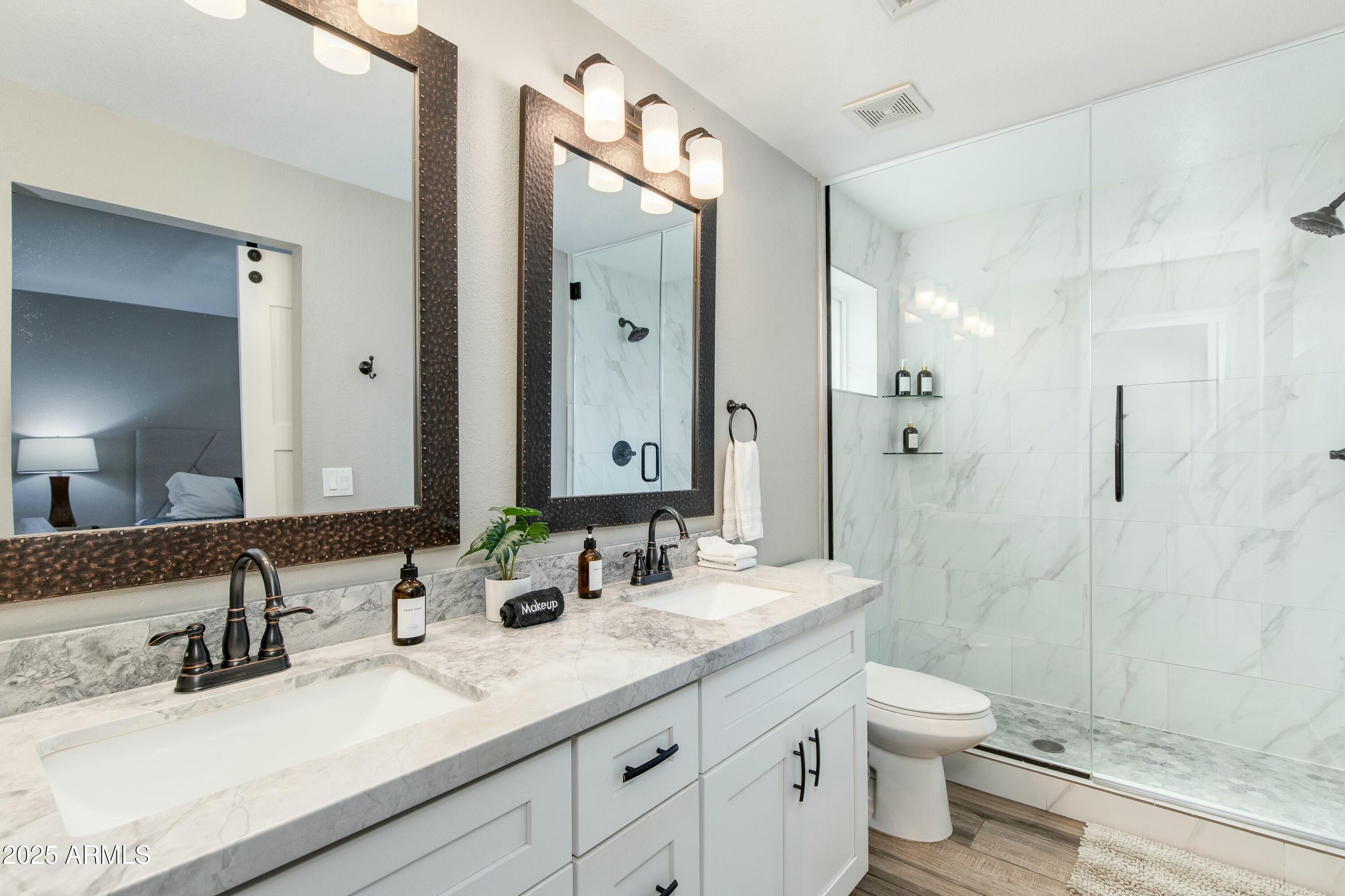 Bathroom with a marble-look double vanity, dark framed mirrors, and a glass-enclosed tiled shower.