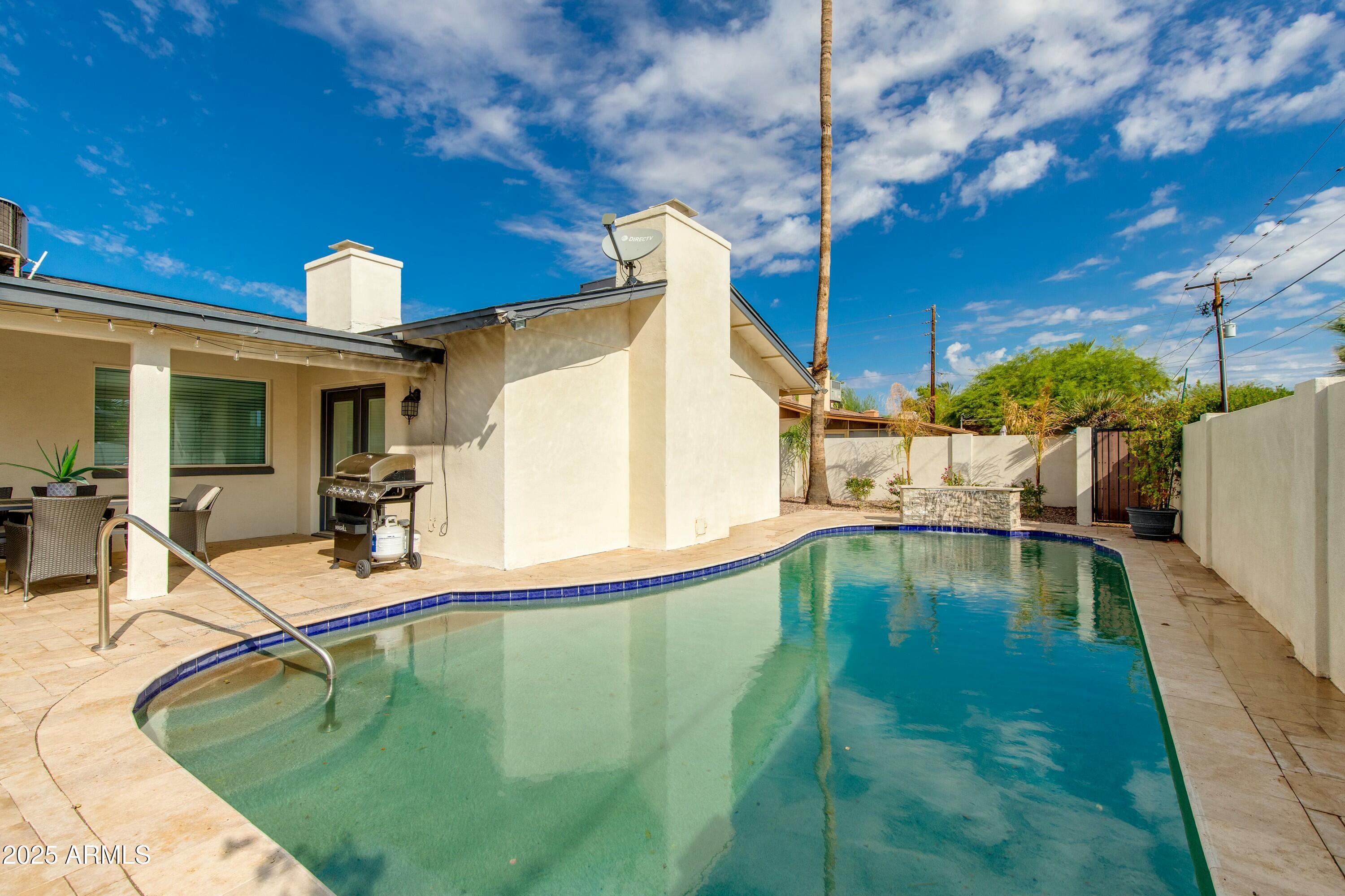 Backyard pool beside a covered patio with outdoor dining and a barbecue grill.
