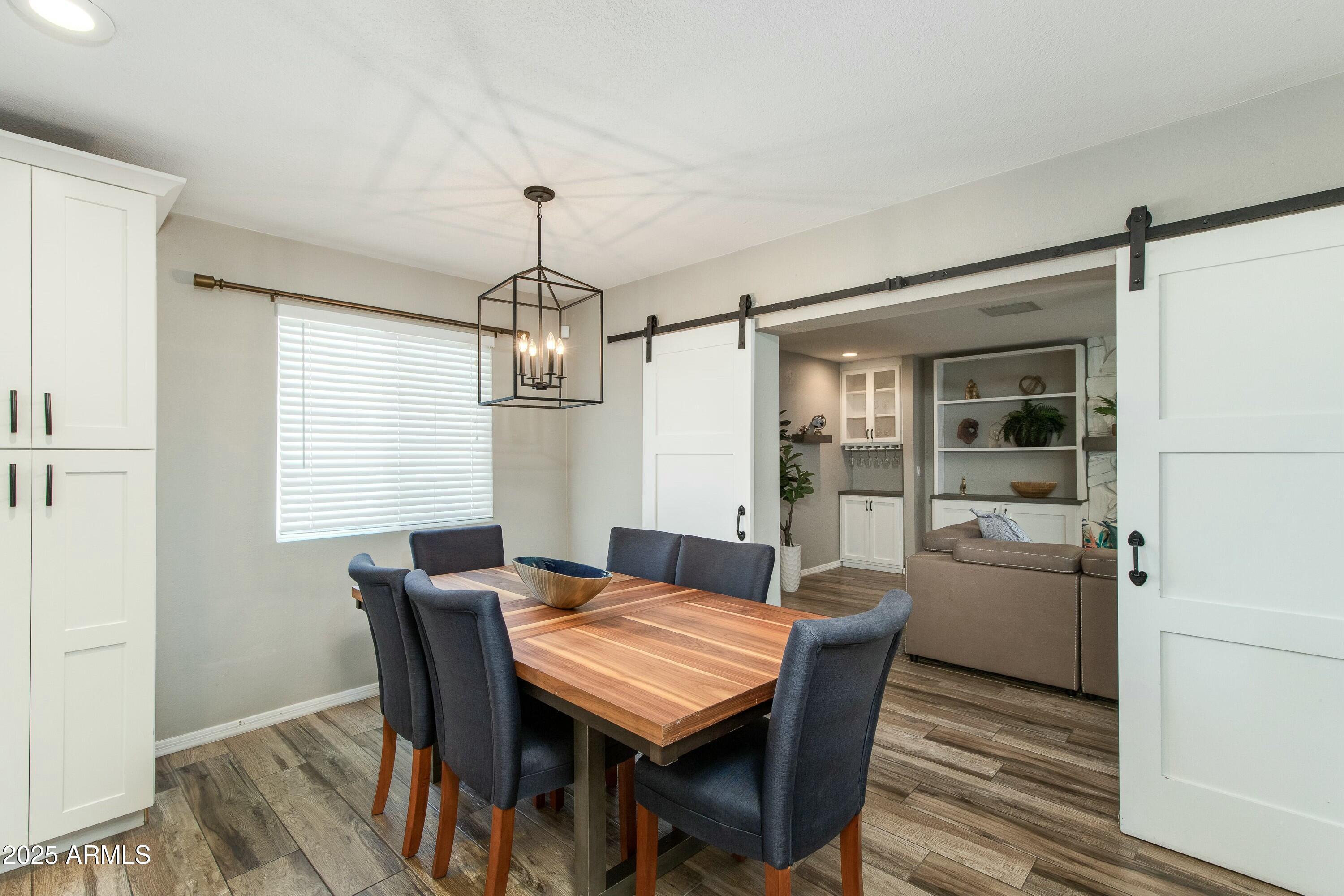 Dining room with a wood table and dark chairs, opening through barn doors to a sitting area.