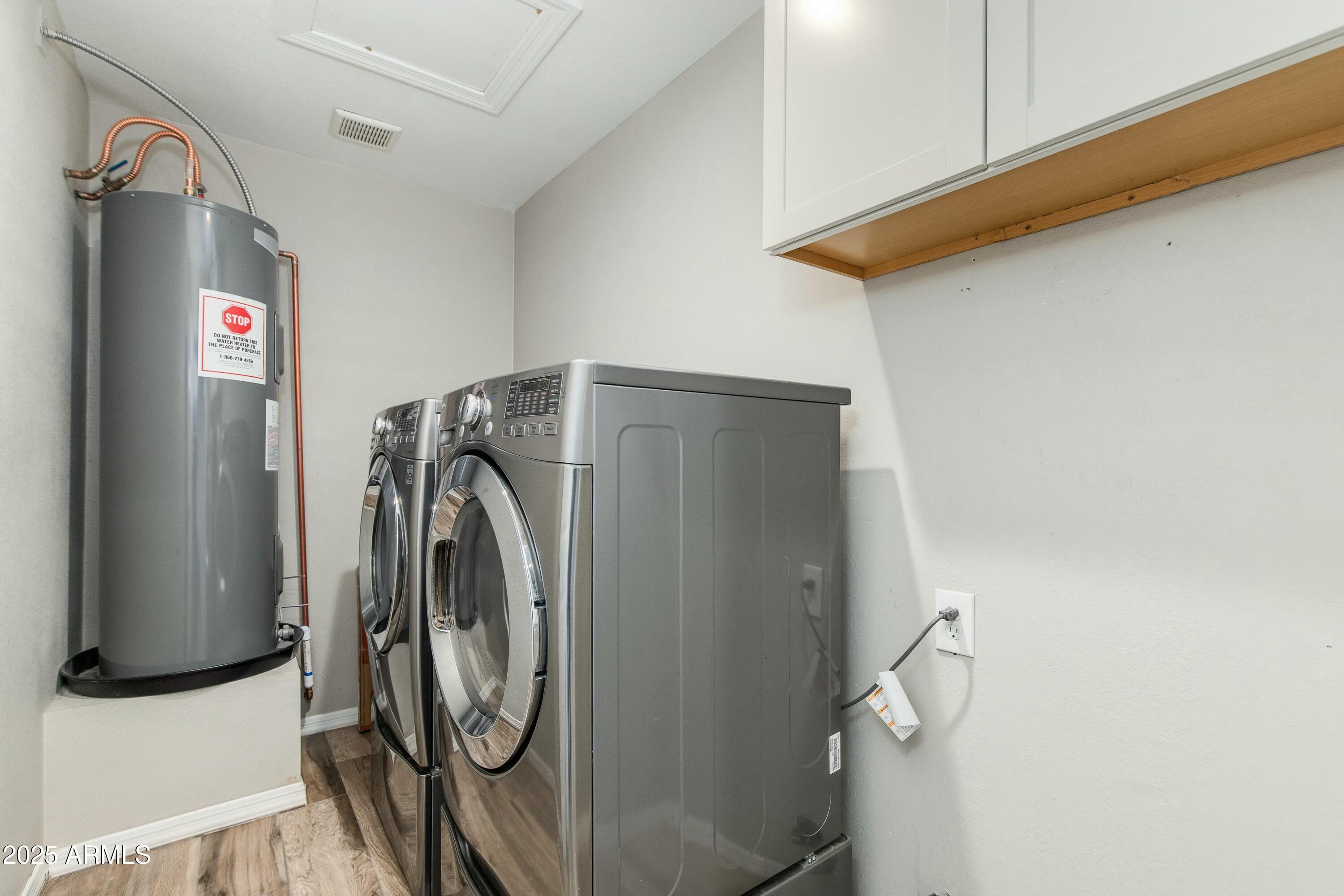 Laundry room with front-loading washer and dryer beside a gray water heater and overhead cabinets.
