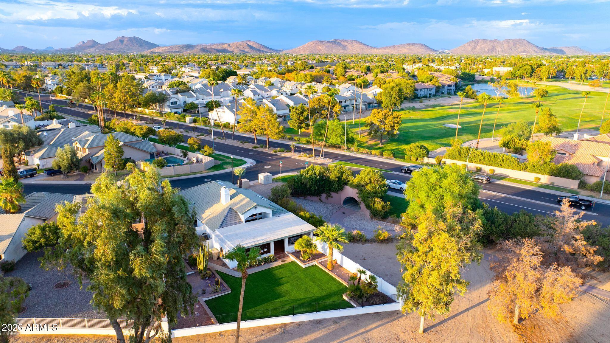 Aerial view of a landscaped home beside a golf course, with mountains beyond.