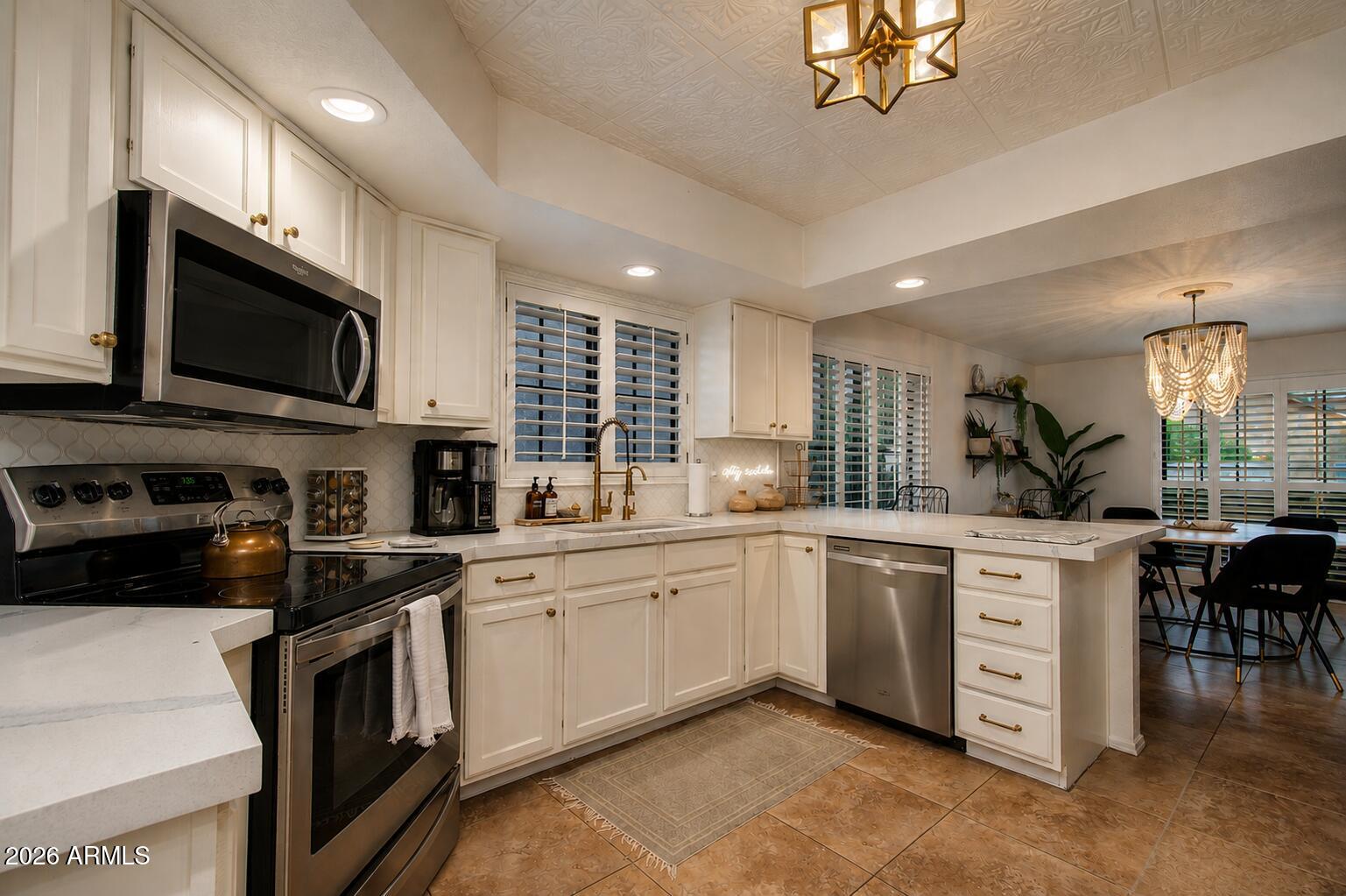 Kitchen with white cabinetry, a large island, stainless steel appliances, and brass fixtures opening to a dining area.