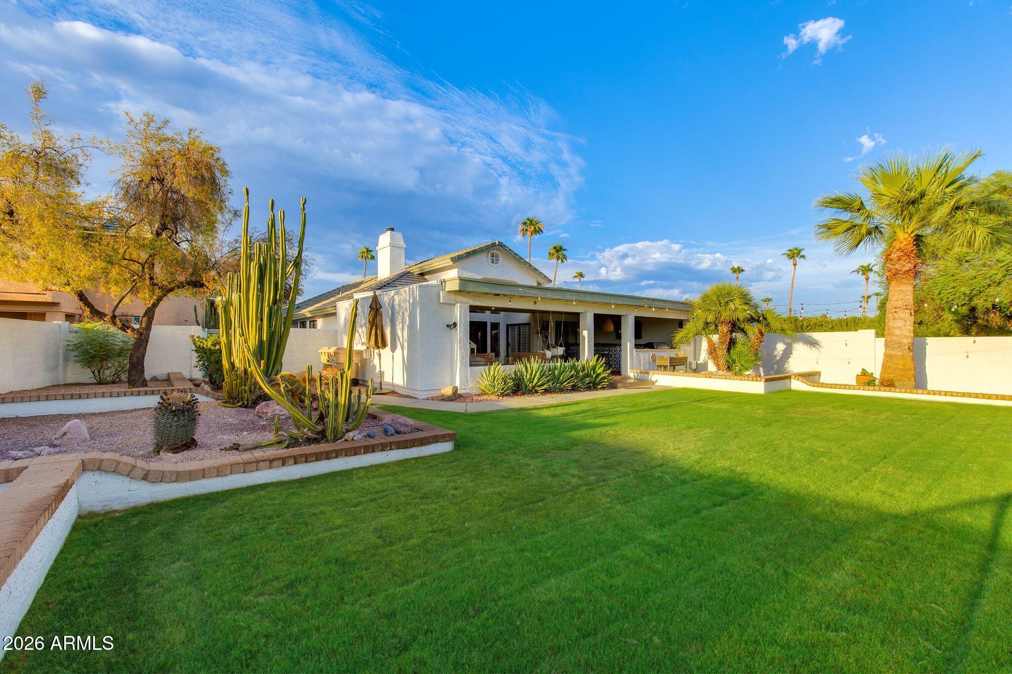Home’s backyard with a covered patio, broad green lawn, and tall cacti.