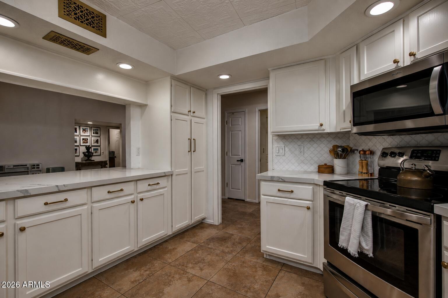 Kitchen with white cabinetry, marble-look counters, patterned backsplash, and stainless steel appliances.