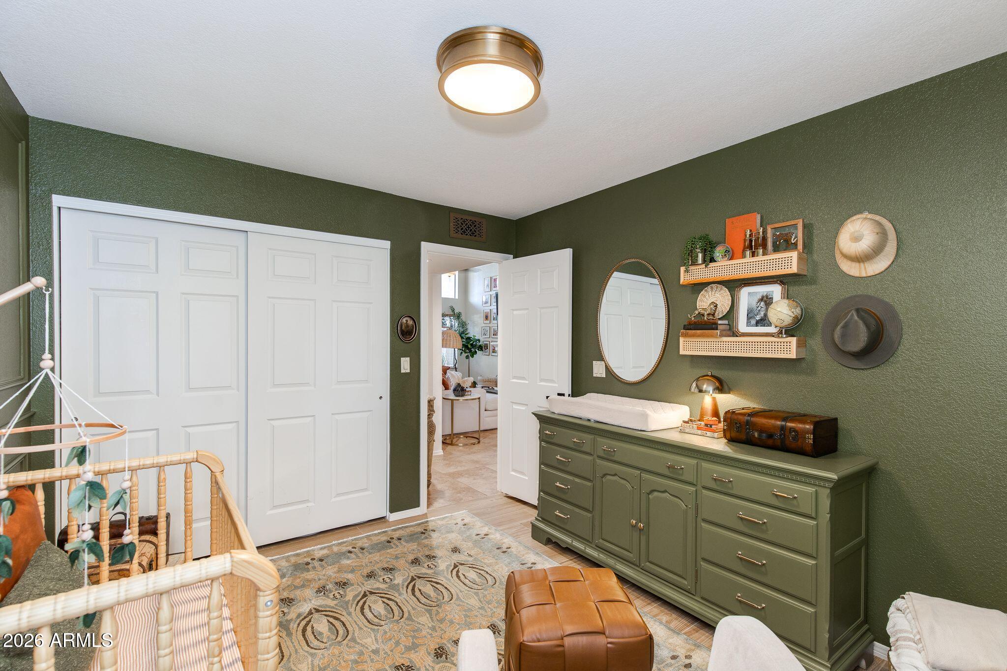 Furnished nursery with a wooden crib, green dresser and walls, white closet doors, and patterned rug.
