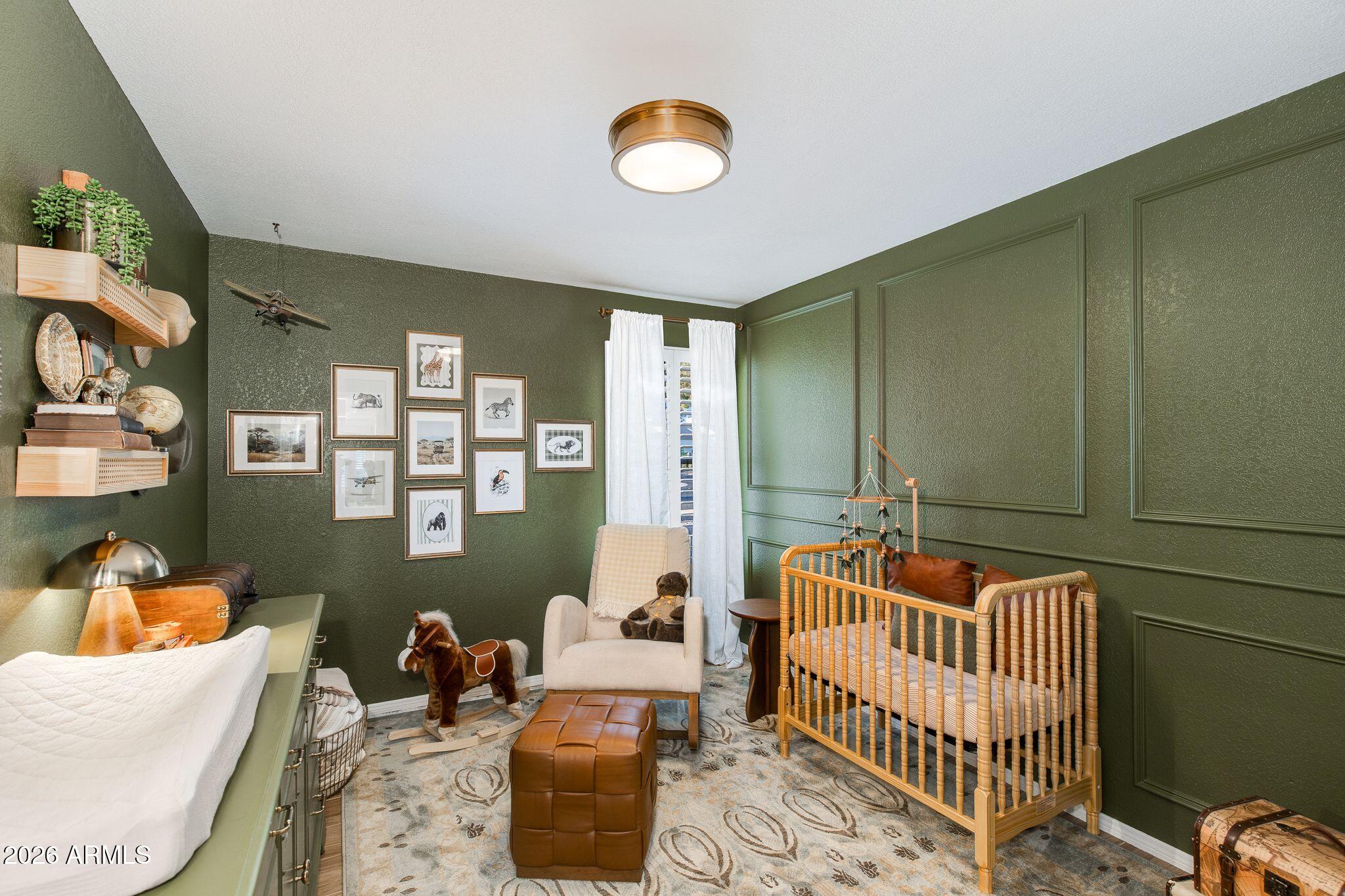 Nursery with a wooden crib, olive-green paneled walls, and horse-themed decor.