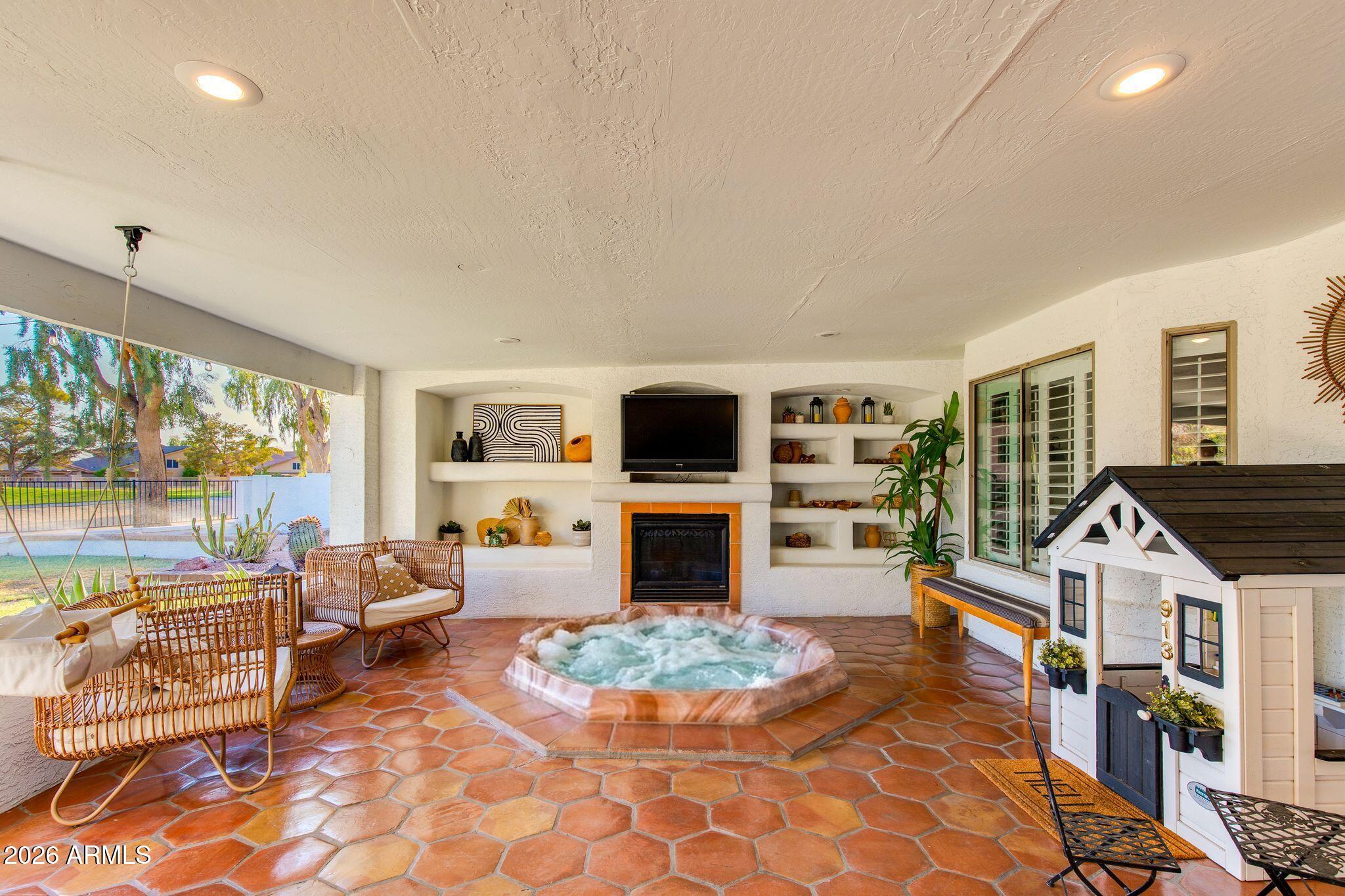 Covered patio with terracotta tile, wicker seating, built-in fireplace, and raised spa.
