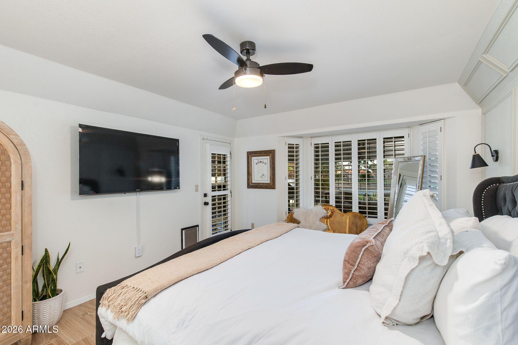 Bedroom with a large bed, plantation shutters, and a ceiling fan.