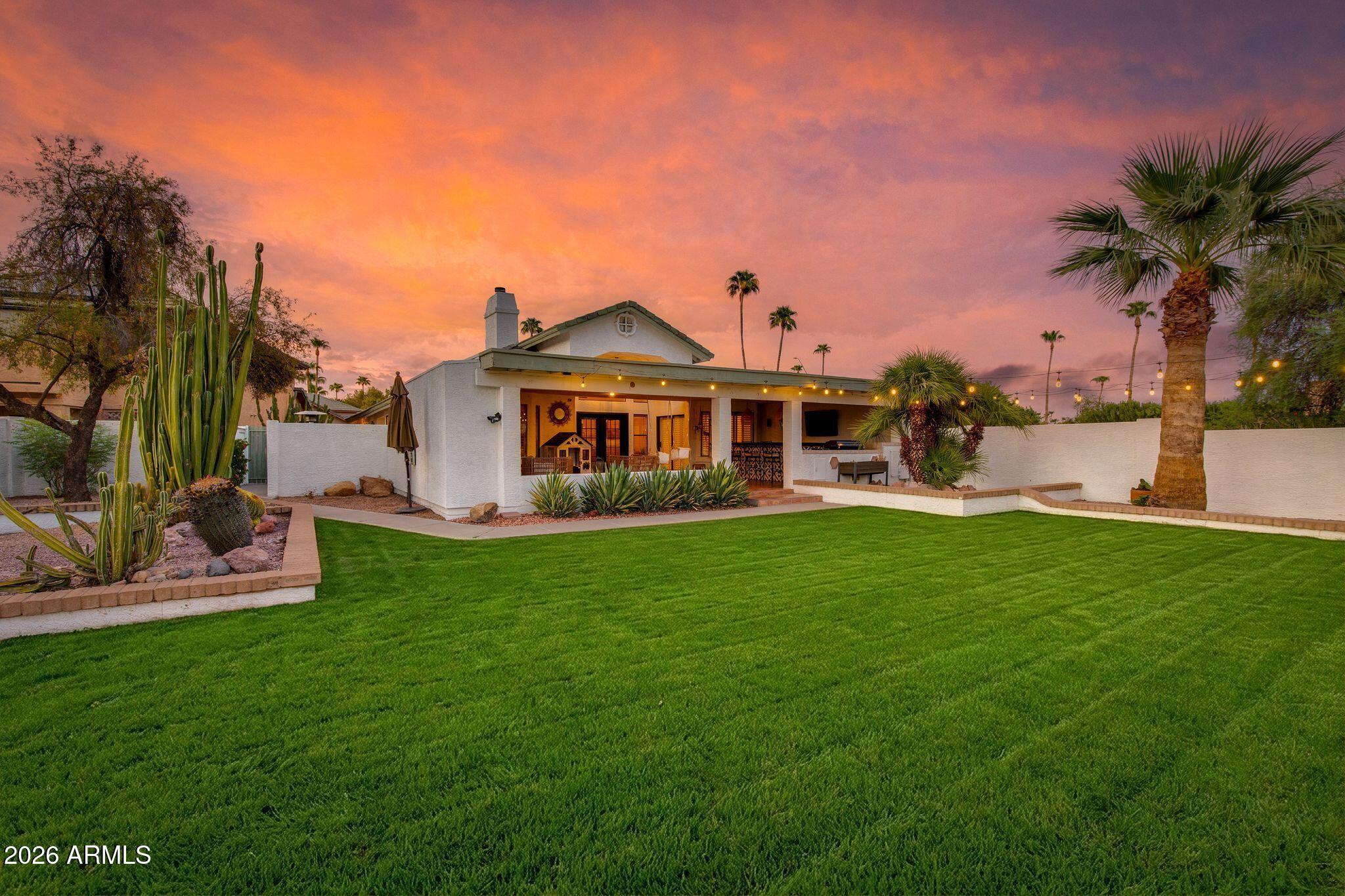 Backyard with a covered patio, broad lawn, desert plants, and a vivid sunset sky.