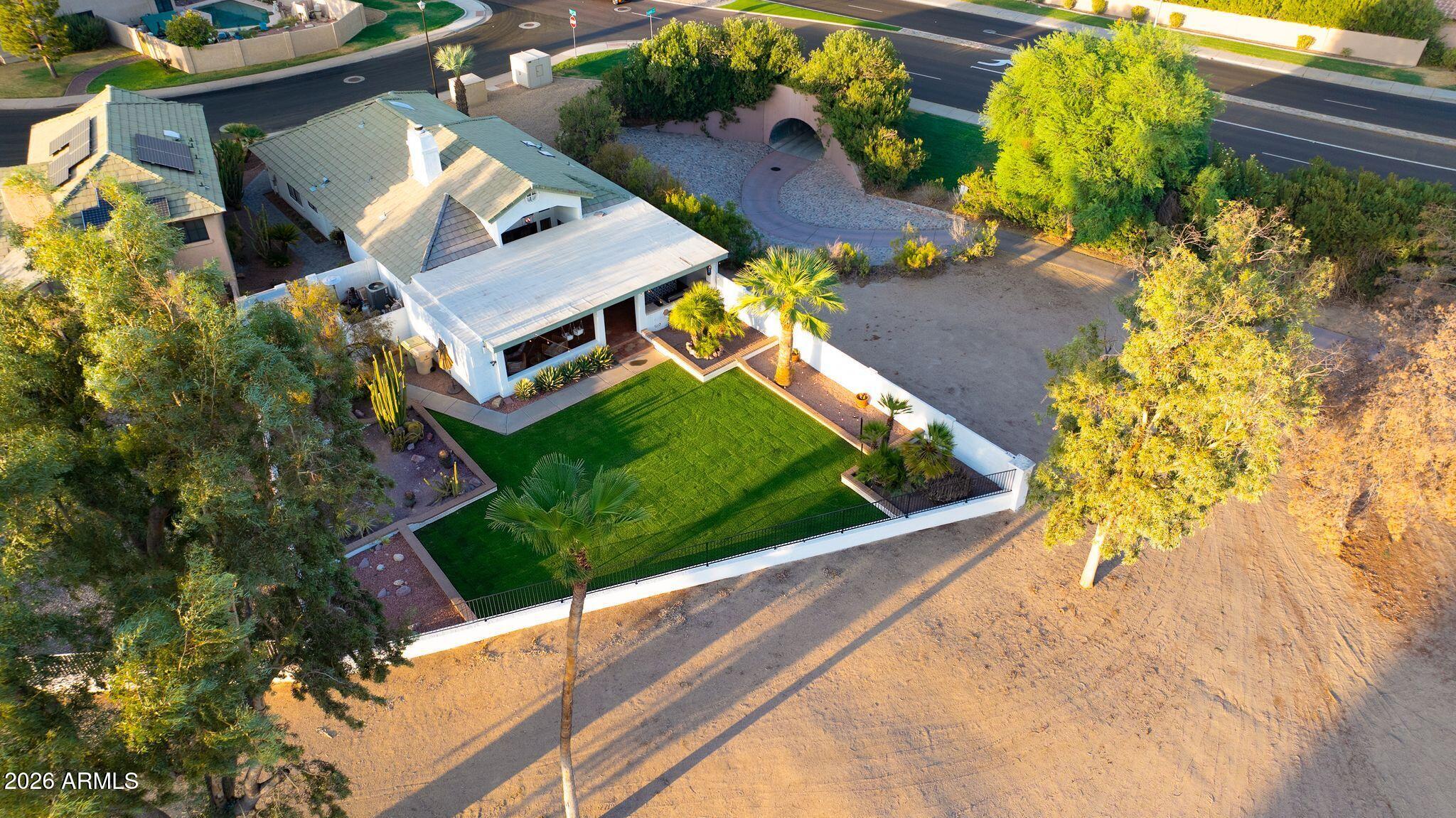 Aerial view of a home with solar panels, covered patio, and fenced artificial-turf yard.