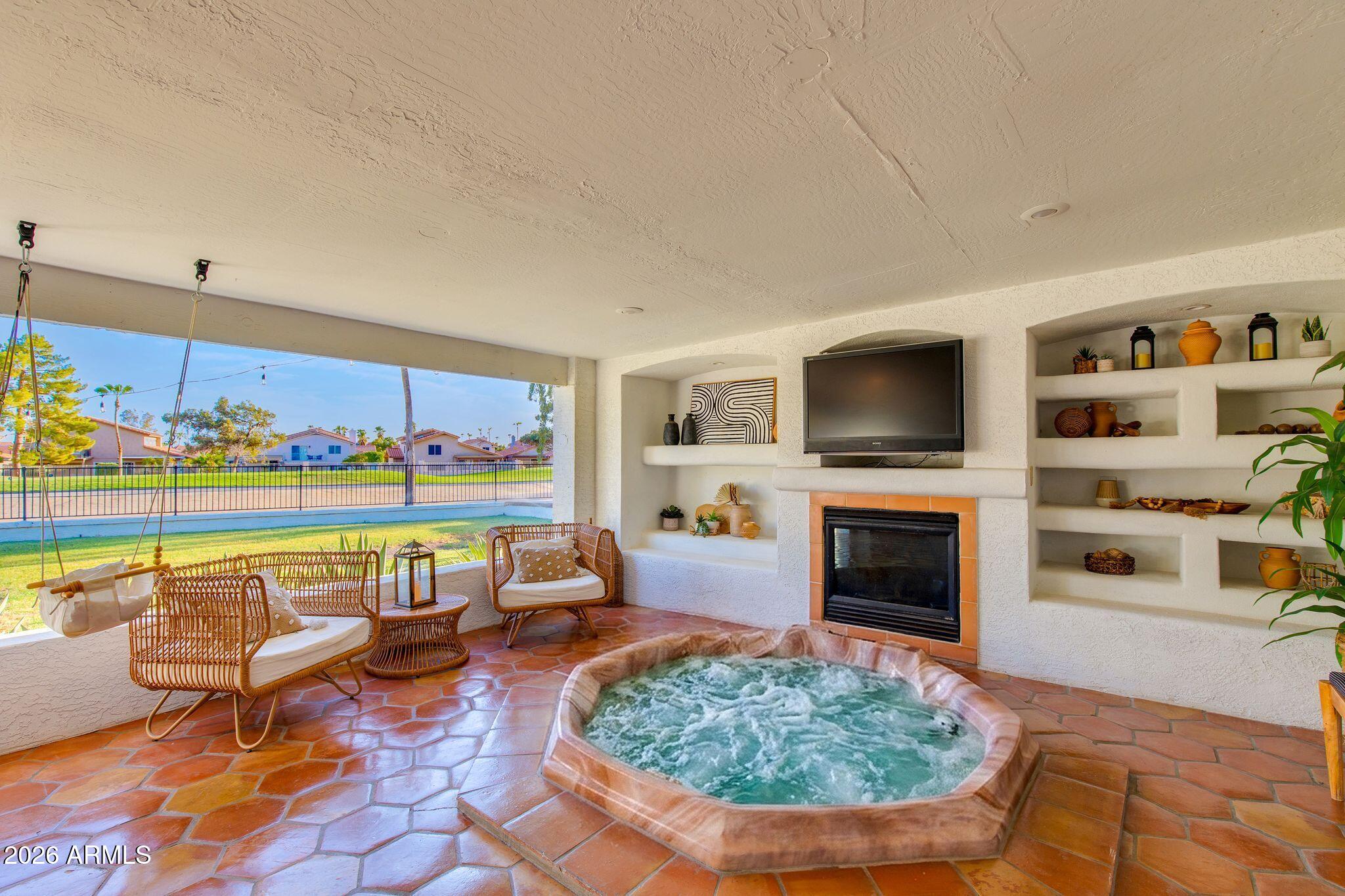 Covered patio with bubbling spa, fireplace, wicker seating, and a view of the fenced yard.
