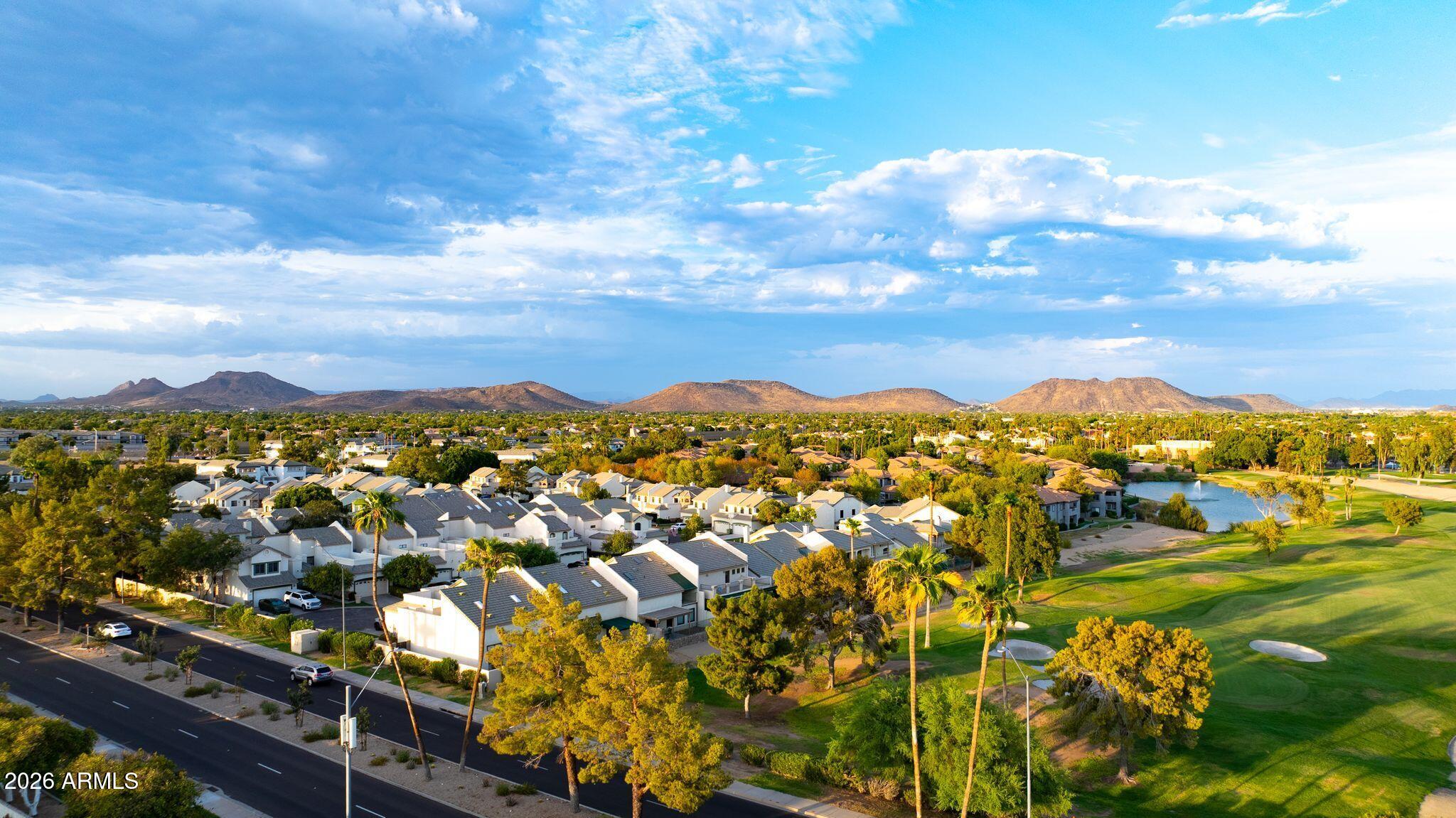 Aerial neighborhood view with a golf course, water feature, and mountains beyond.