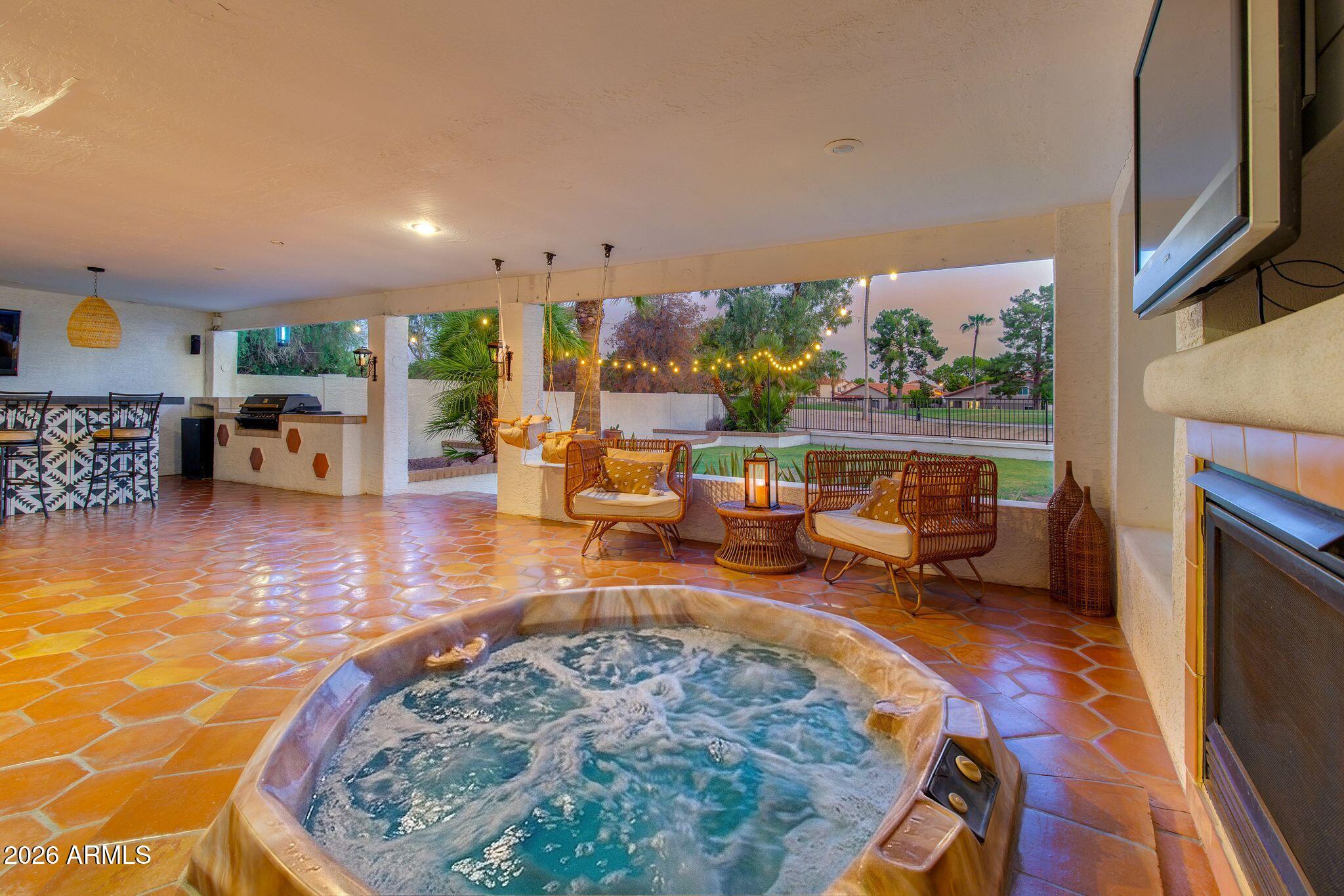 Covered patio with a bubbling hot tub, wicker seating, string lights, and an outdoor bar.