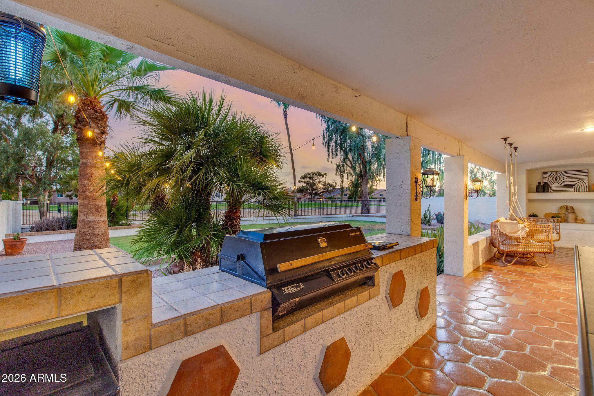 Covered patio with built-in grill, terracotta tile, wicker dining set, and palm trees at dusk.