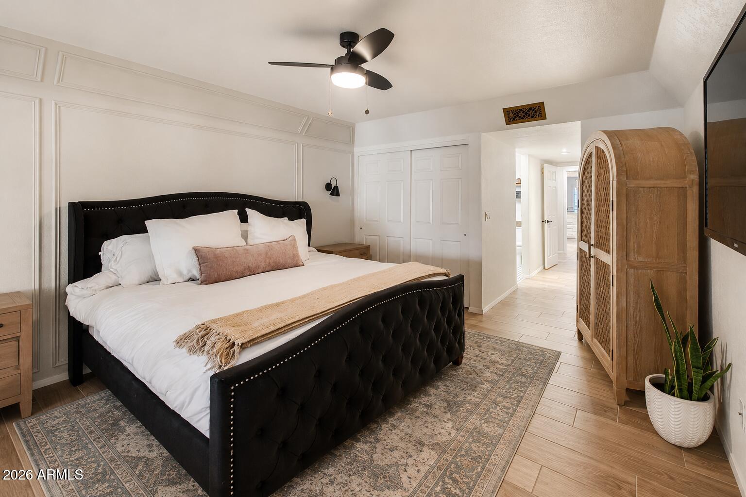 Bedroom with a black tufted bed, white bedding, paneled walls, and a wooden armoire.