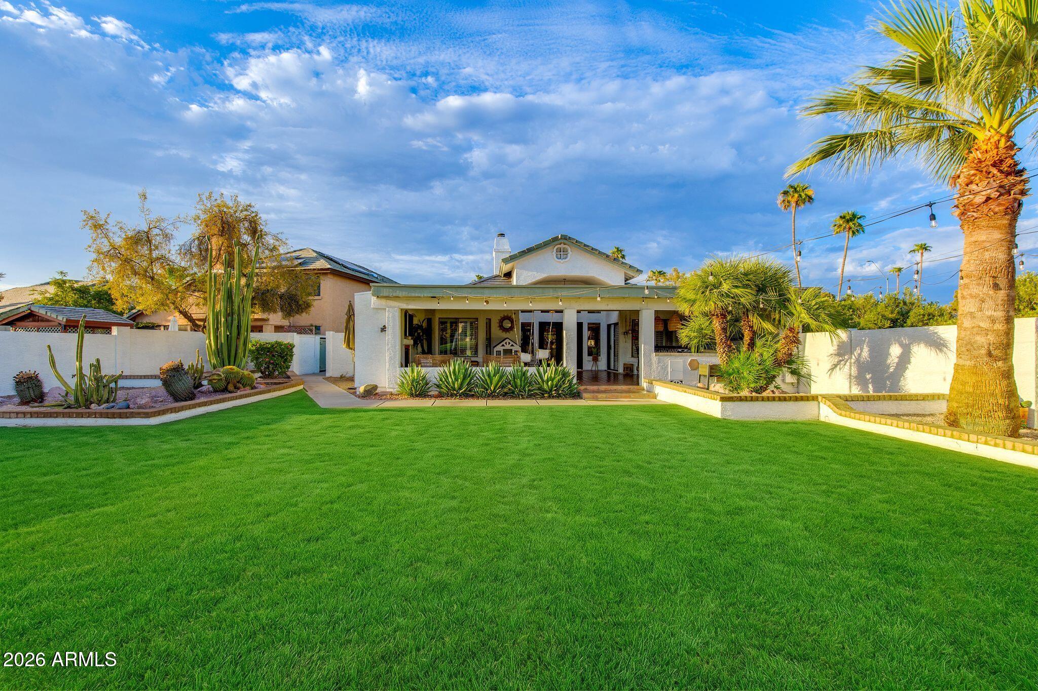 Rear exterior of a home with a covered patio, broad lawn, palms, and desert landscaping.