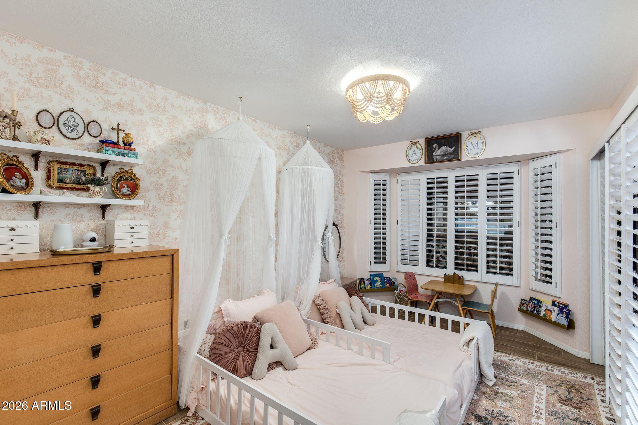 Bedroom with two white canopy beds, pink bedding, plantation shutters, and a wooden dresser.