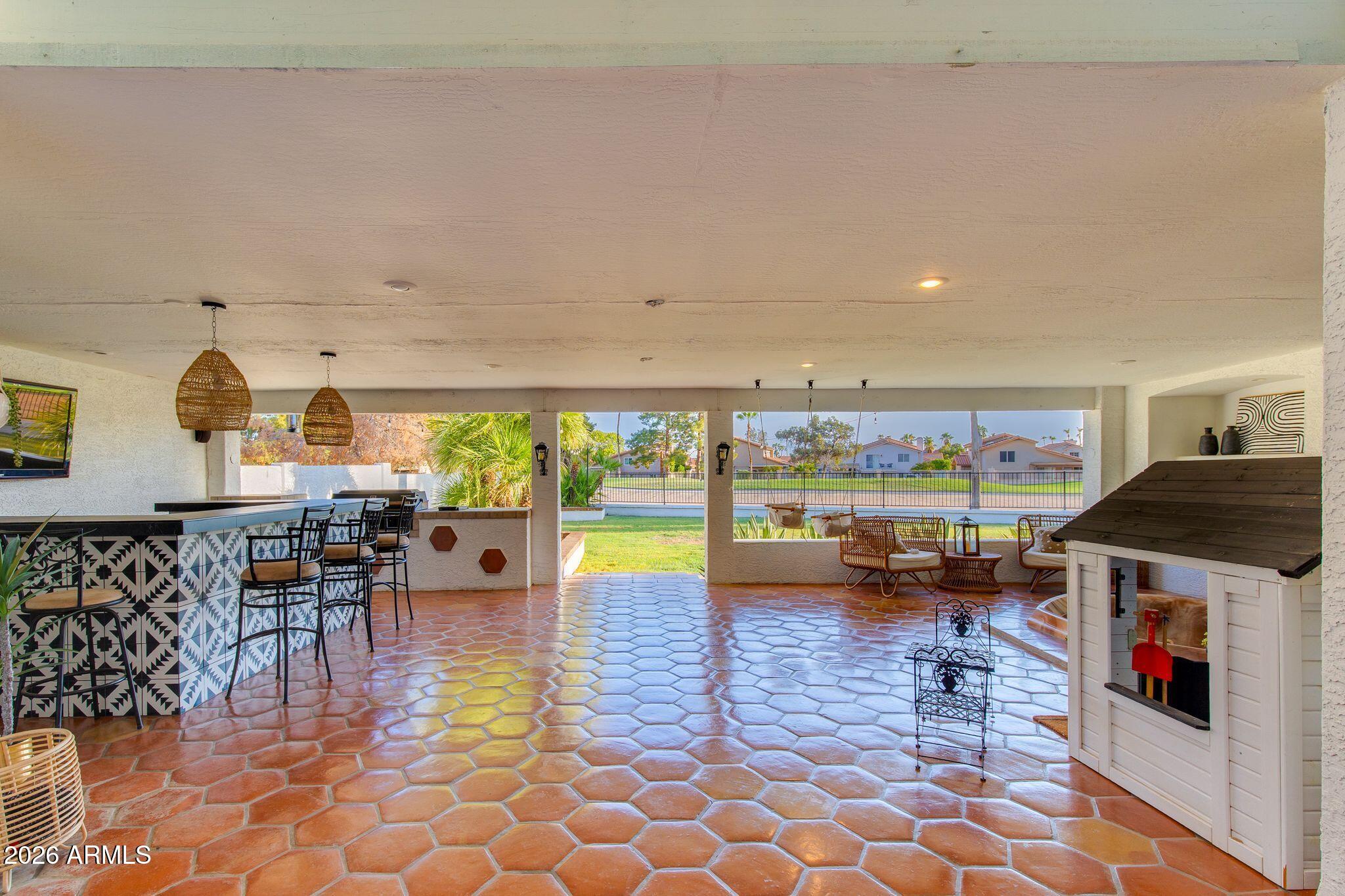 Covered patio with terracotta tile, patterned bar, wicker seating, and views of the backyard.