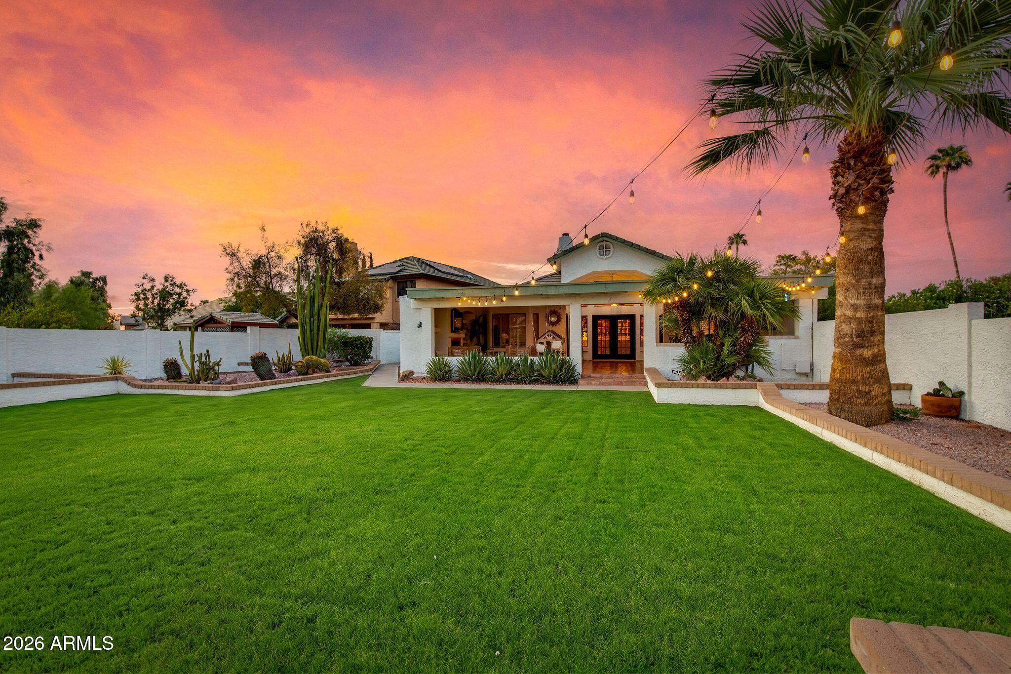Rear of a stucco home with a broad lawn, desert landscaping, and patio string lights at dusk.