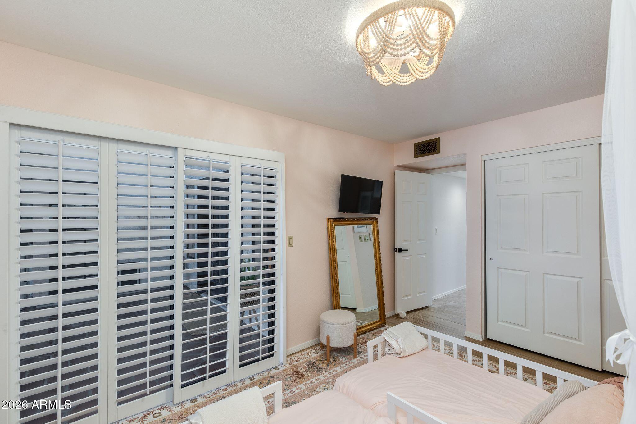 Furnished bedroom with twin beds, plantation shutters, and a beaded ceiling light.
