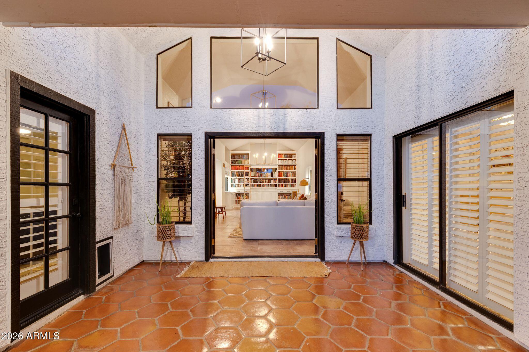 Covered courtyard with terracotta tile floors and open doors framing a living room with bookshelves.