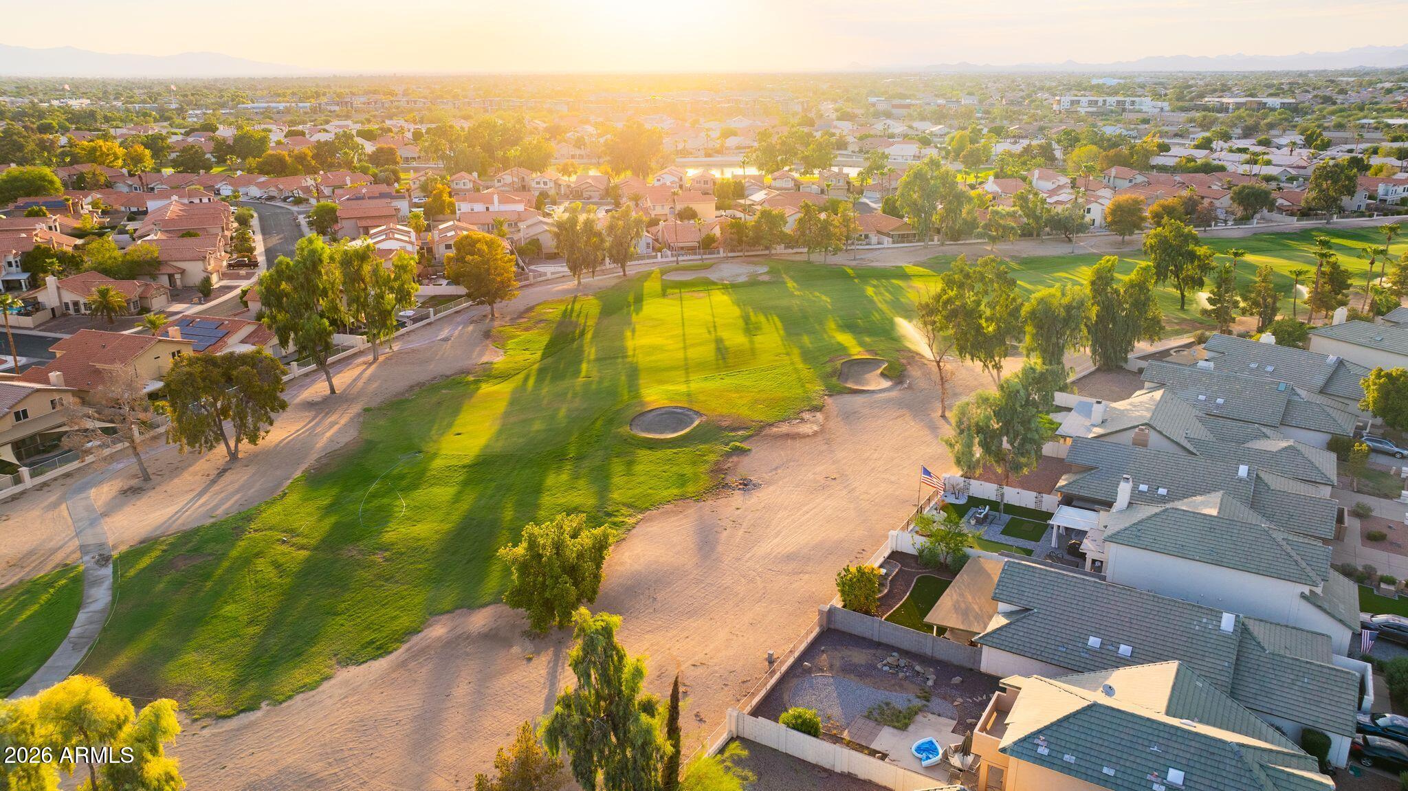 Aerial view of a golf course and surrounding homes, with mountains on the horizon at sunset.
