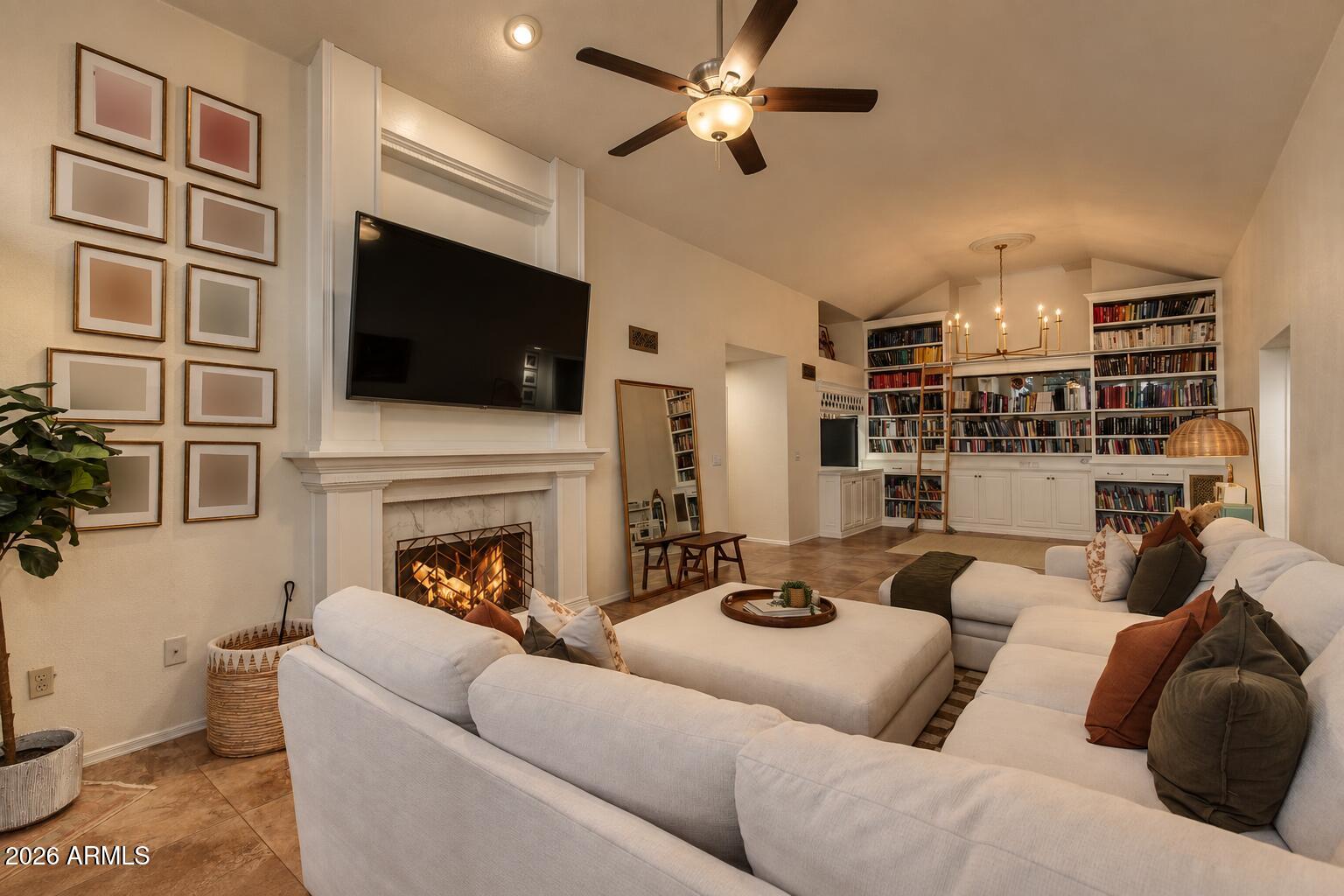 Living room with a white sectional, lit fireplace, wall-mounted television, and built-in bookshelves.