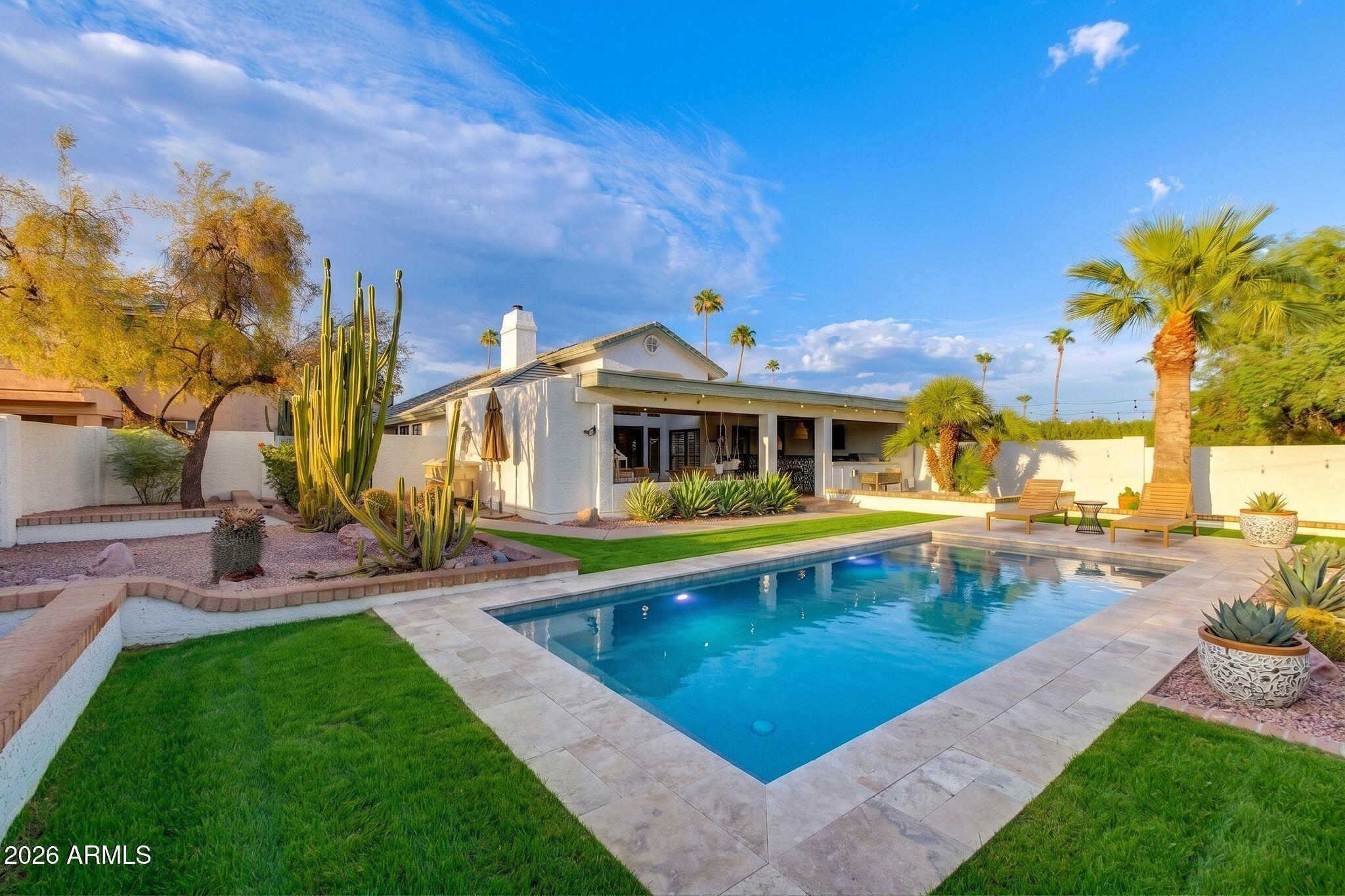 Backyard pool beside a covered patio, with desert landscaping and palm trees.