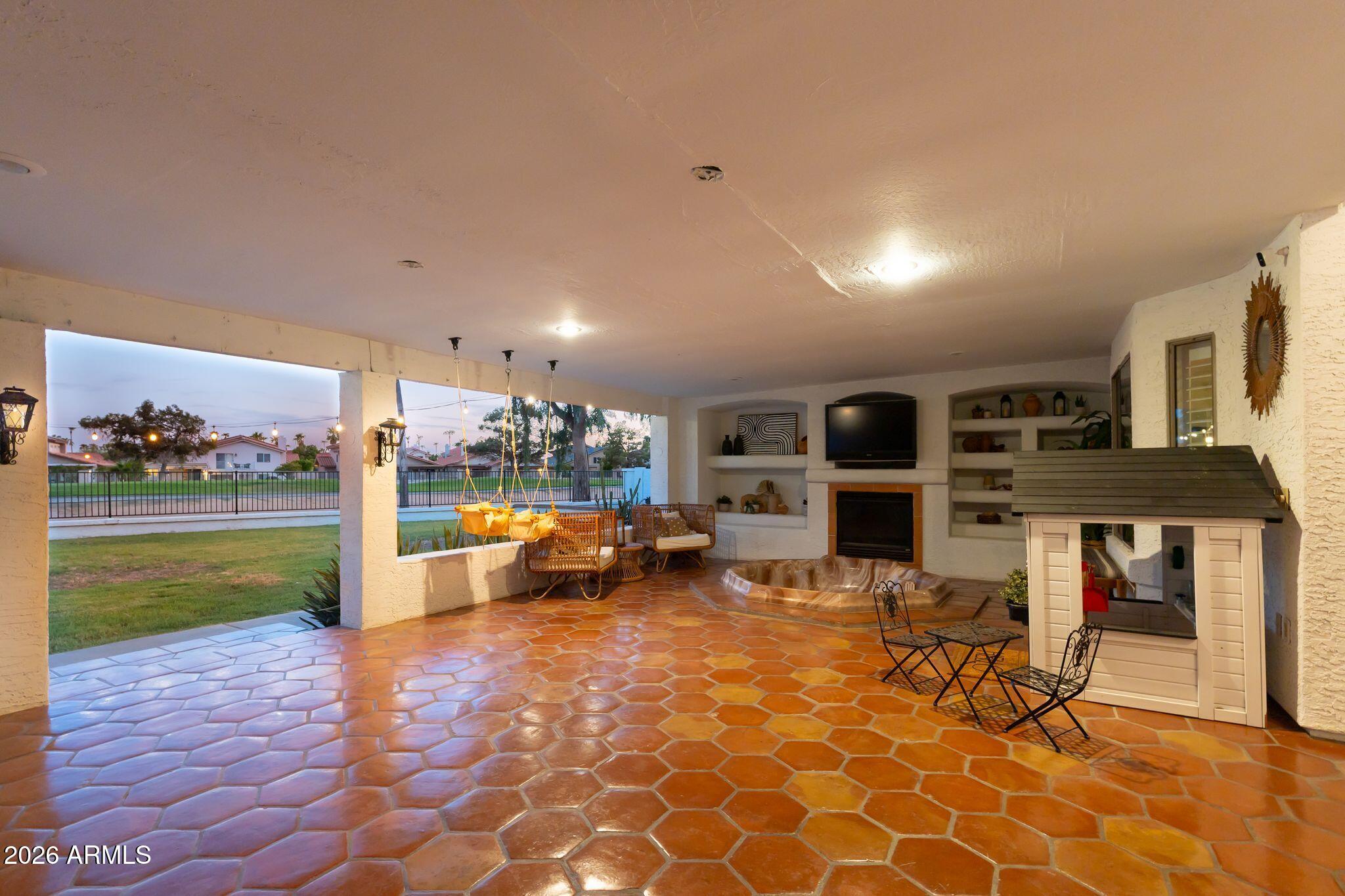 Covered patio with terracotta tile, hanging swings, fireplace, spa, and fenced grassy yard.