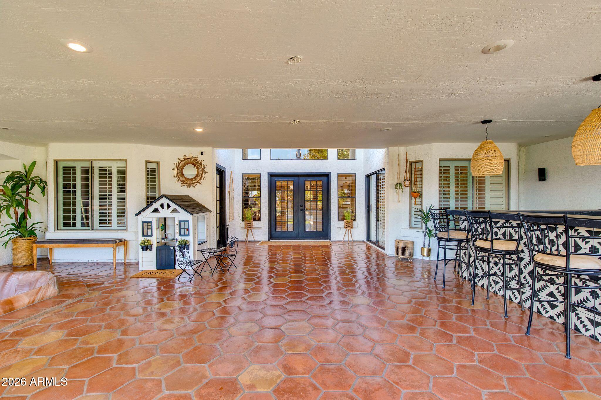Covered patio with terracotta tile, dark double doors, and a bar with stools.