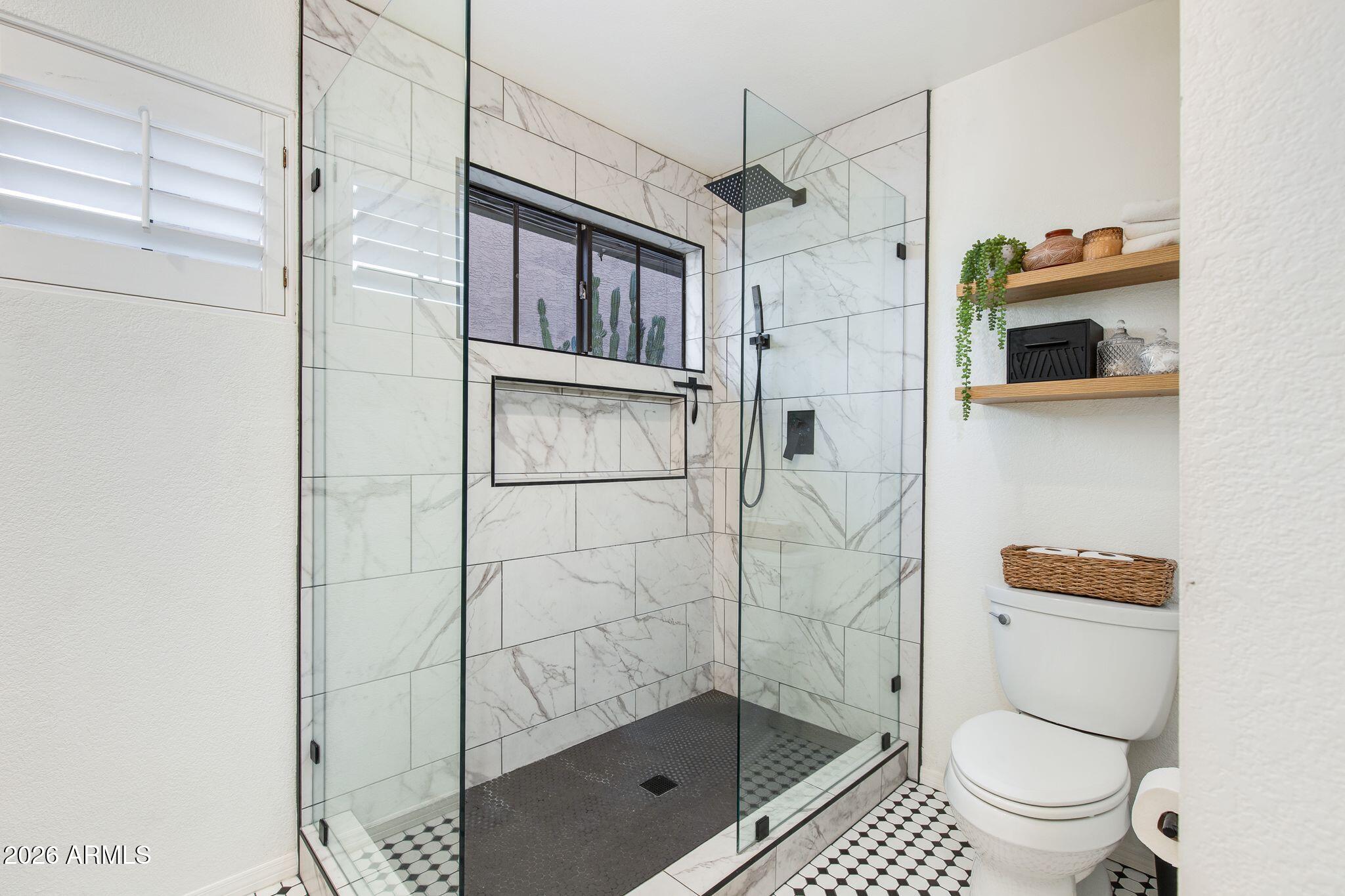 Bathroom with a glass-enclosed marble-look shower, black fixtures, and black-and-white hex tile floor.