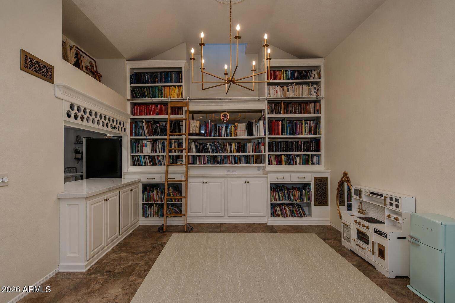 Library with floor-to-ceiling bookcases, a rolling ladder, and a child-sized play kitchen.